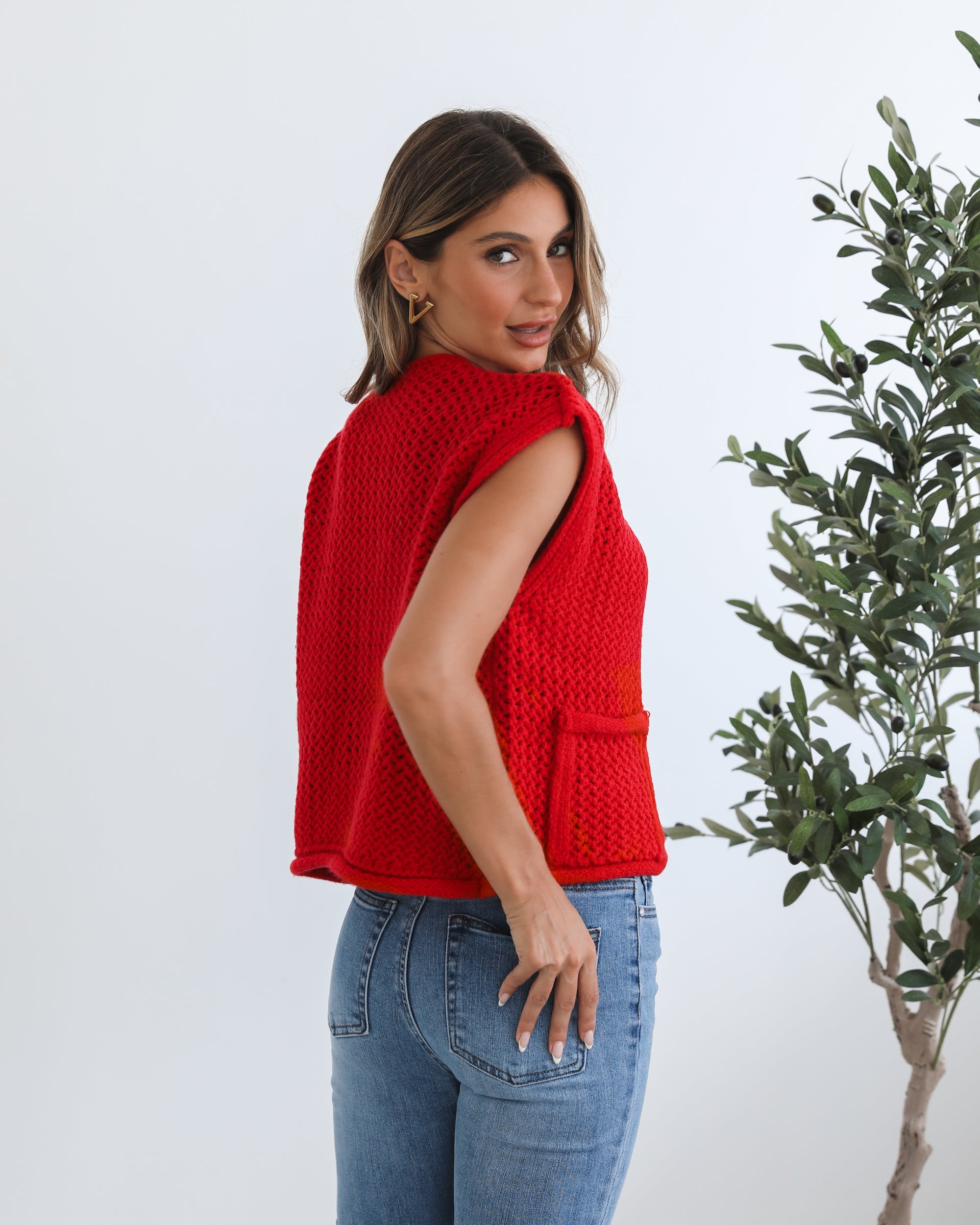 A woman wearing a red knit top with round neckline and center-front buttons, paired with blue jeans.