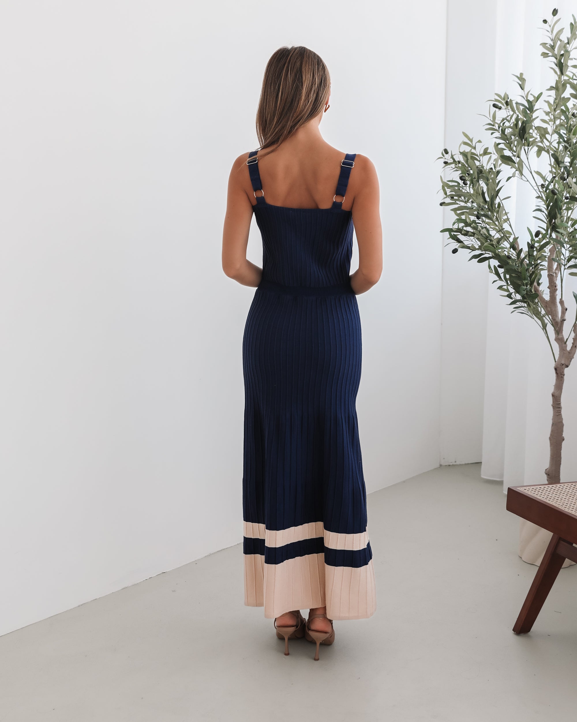 A navy and beige toned dress with thin straps and a square neckline. The dress has a fit-and-flare silhouette and reaches mid-calf in length.