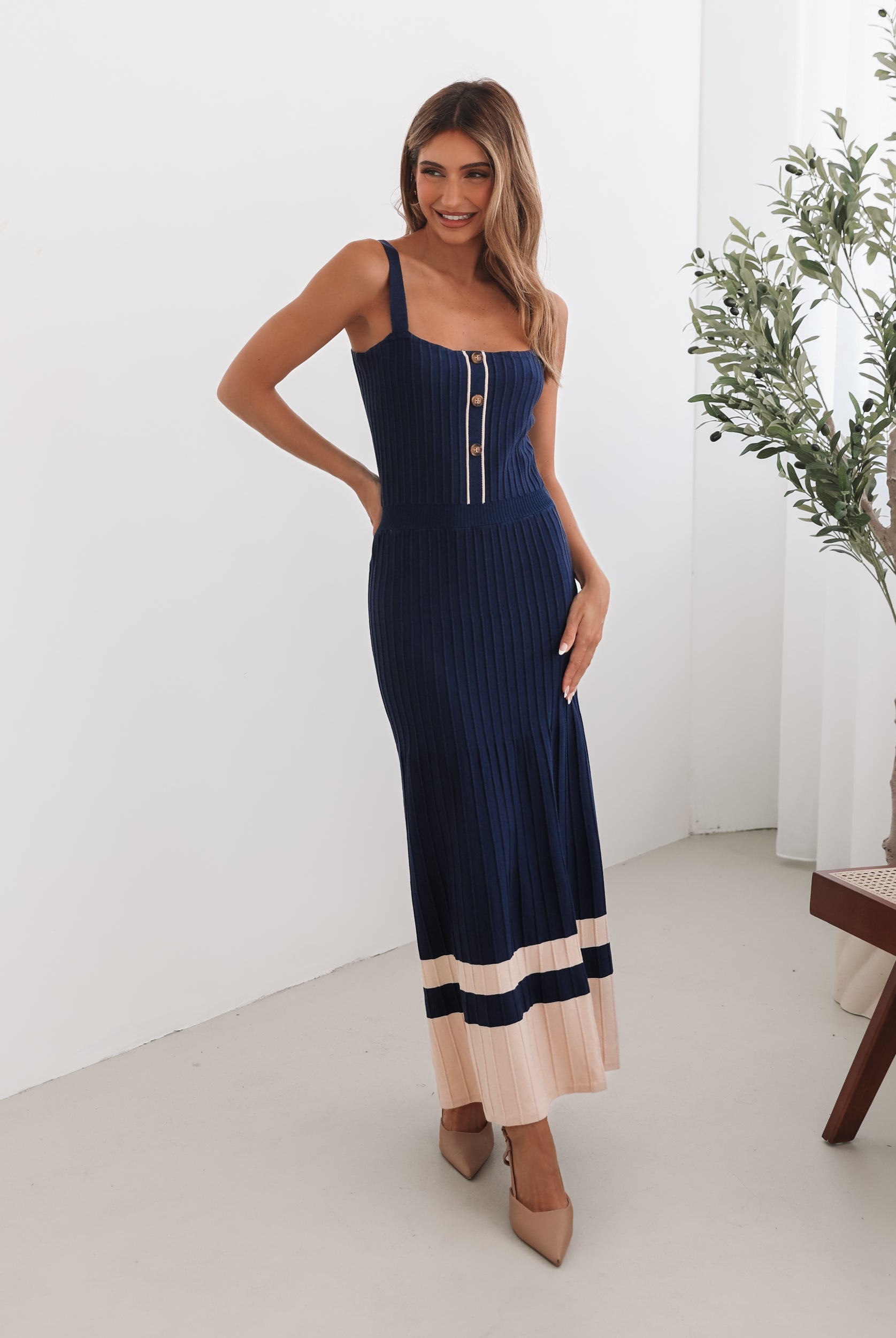 A navy and beige toned dress with thin straps and a square neckline. The dress has a fit-and-flare silhouette and reaches mid-calf in length.