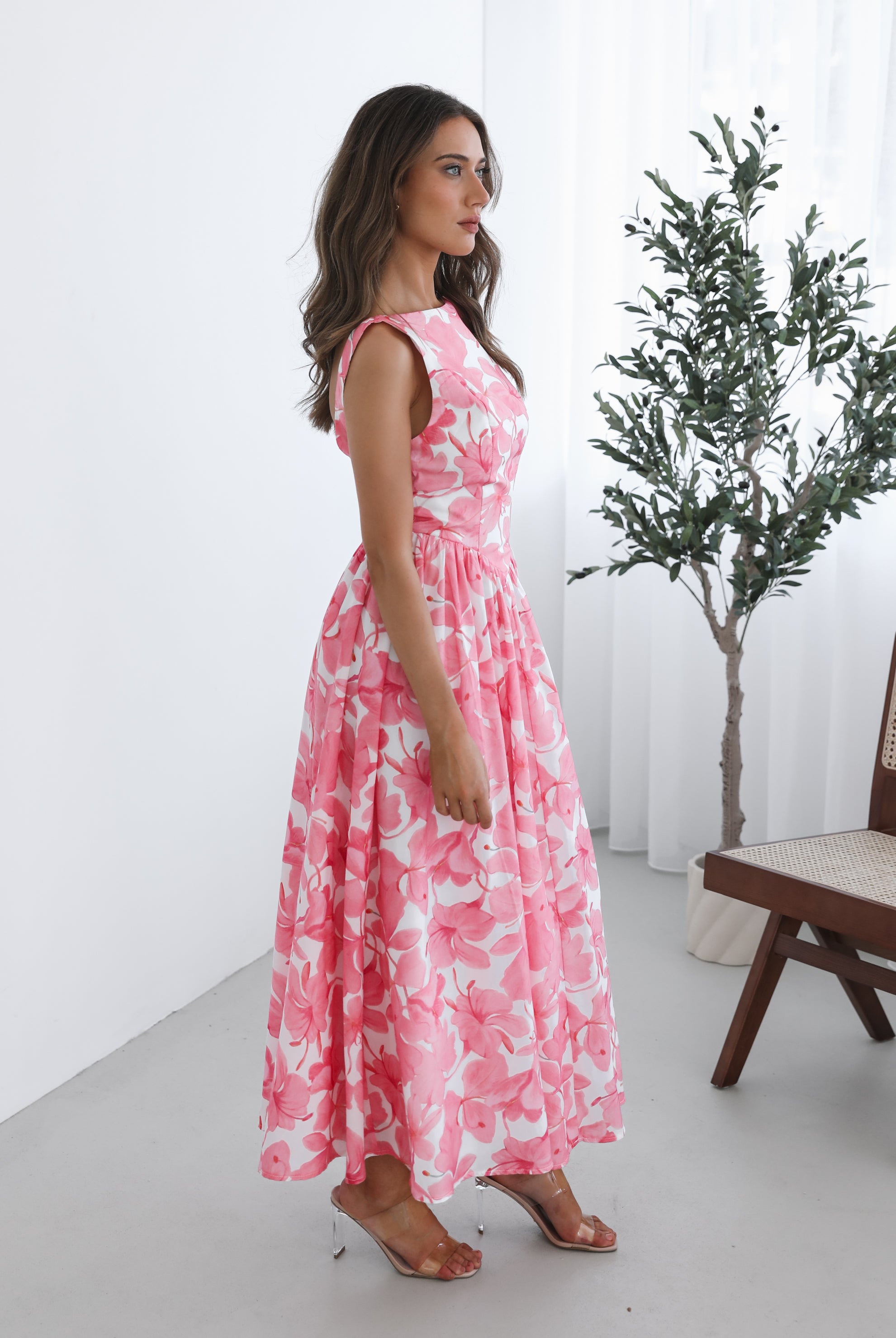 A woman wearing a pink floral maxi dress with a boat neckline and a flowy skirt.