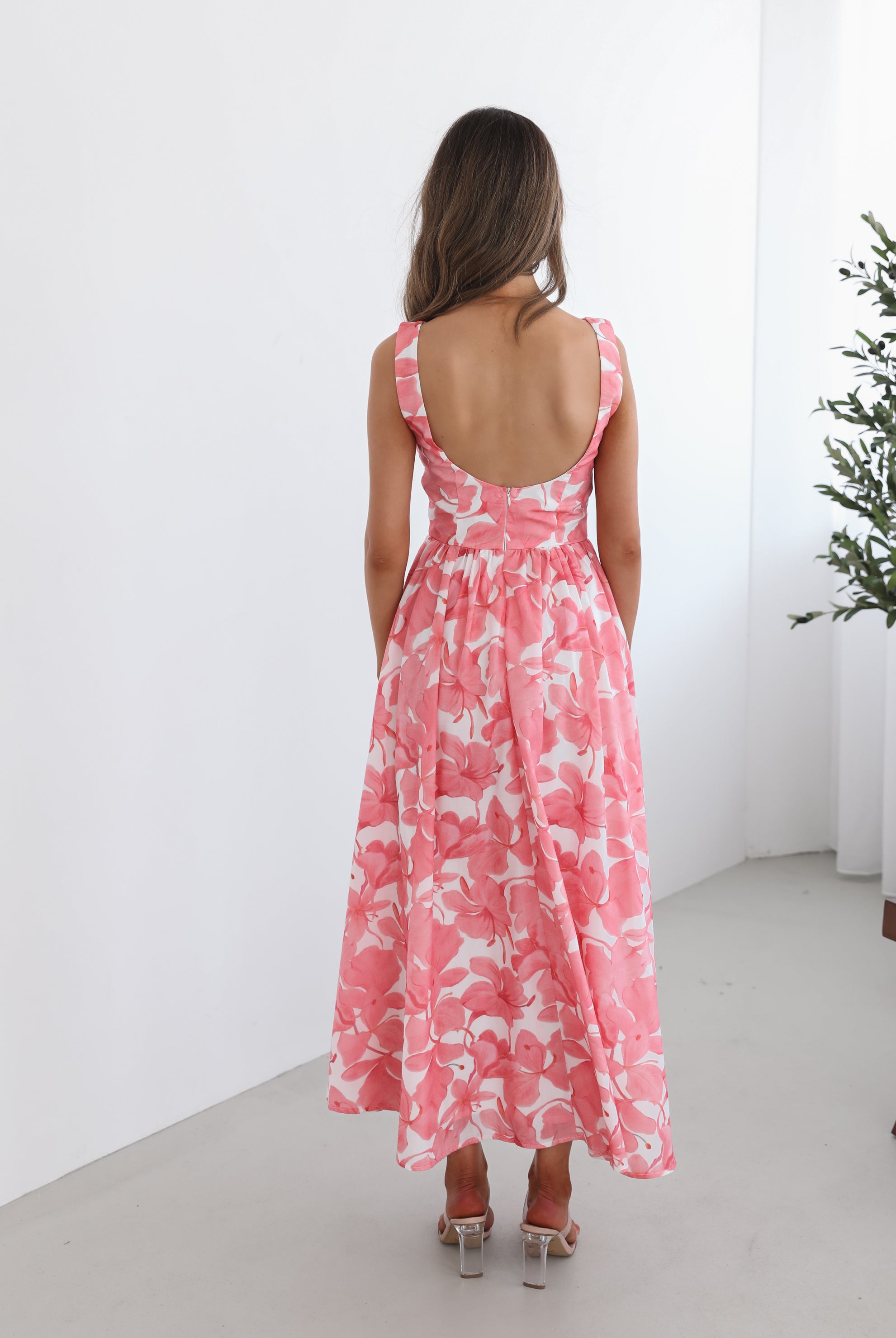 A woman wearing a pink floral maxi dress with a boat neckline and a flowy skirt.