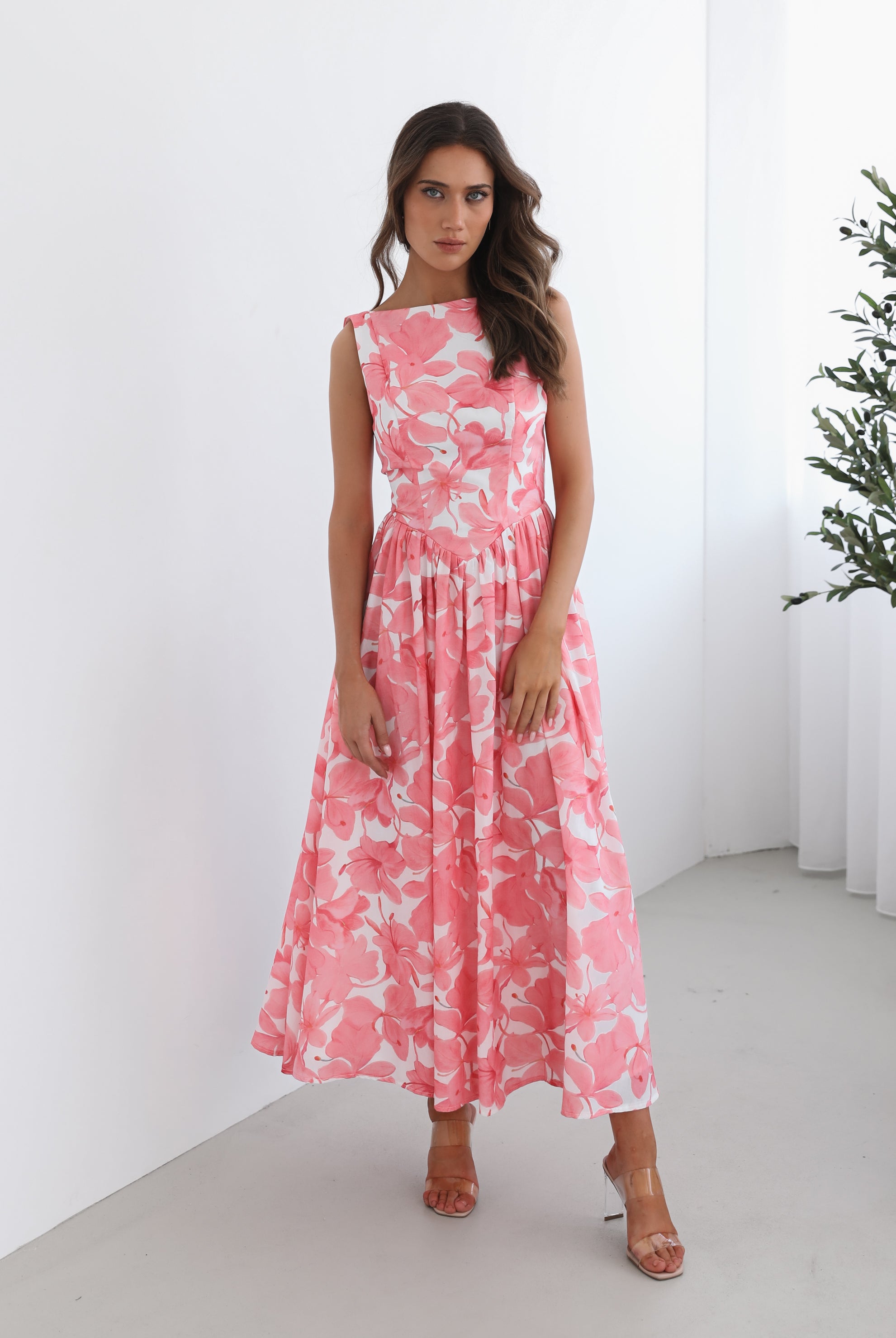 A woman wearing a pink floral maxi dress with a boat neckline and a flowy skirt.