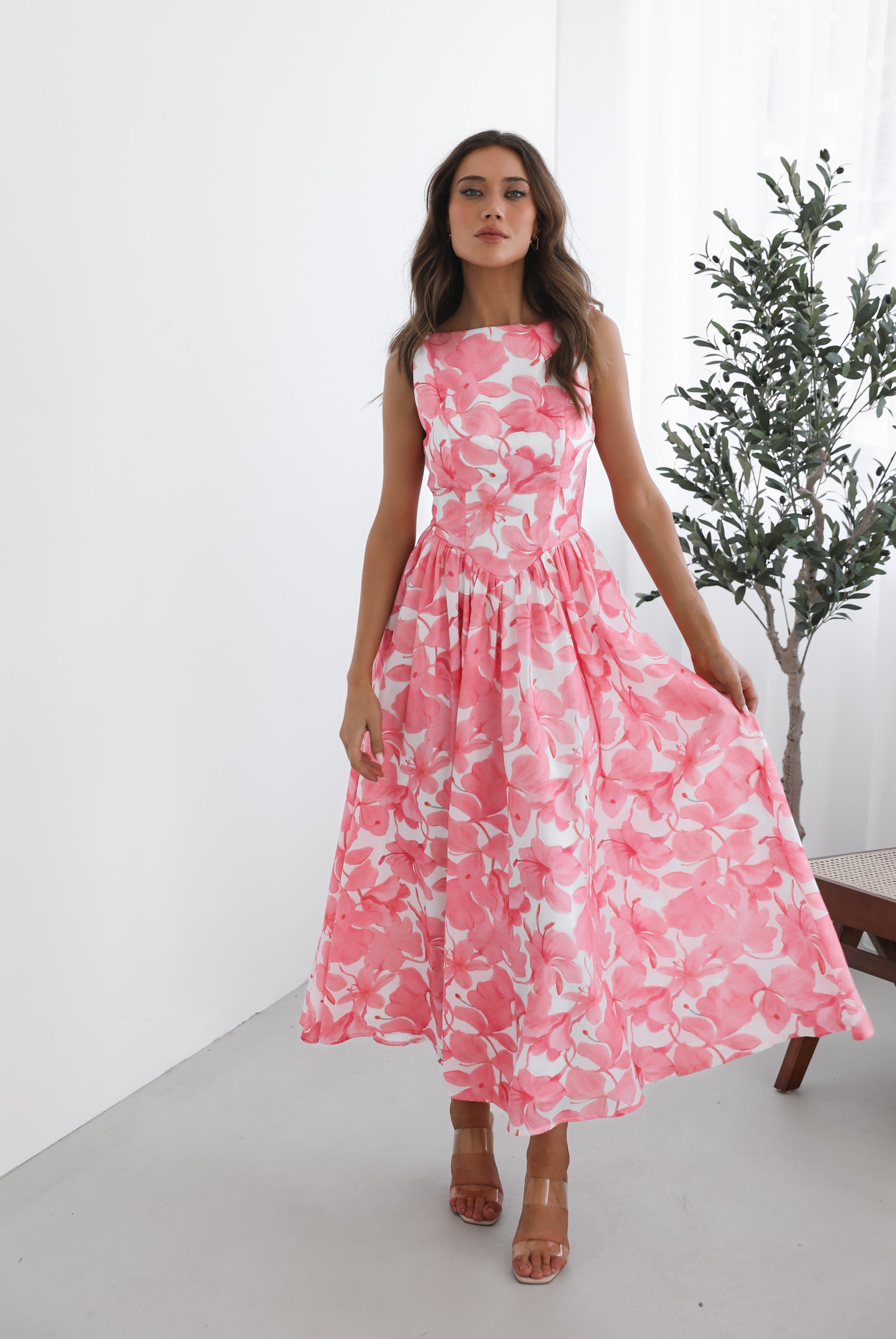 A woman wearing a pink floral maxi dress with a boat neckline and a flowy skirt.