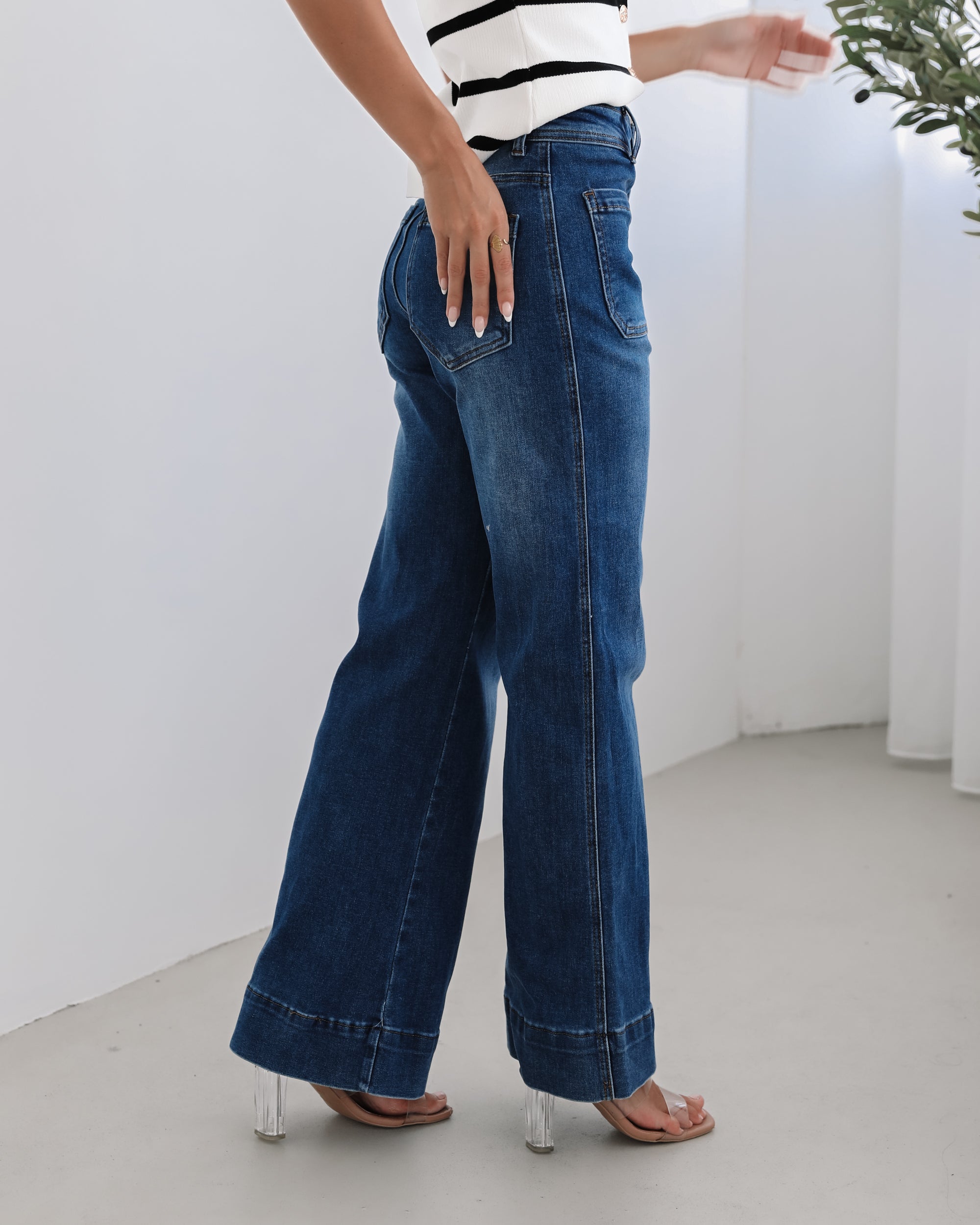 A woman standing in a room with light decor, wearing a striped top and mid-blue Yzabel Jeans with a high waist fit and wide leg silhouette.