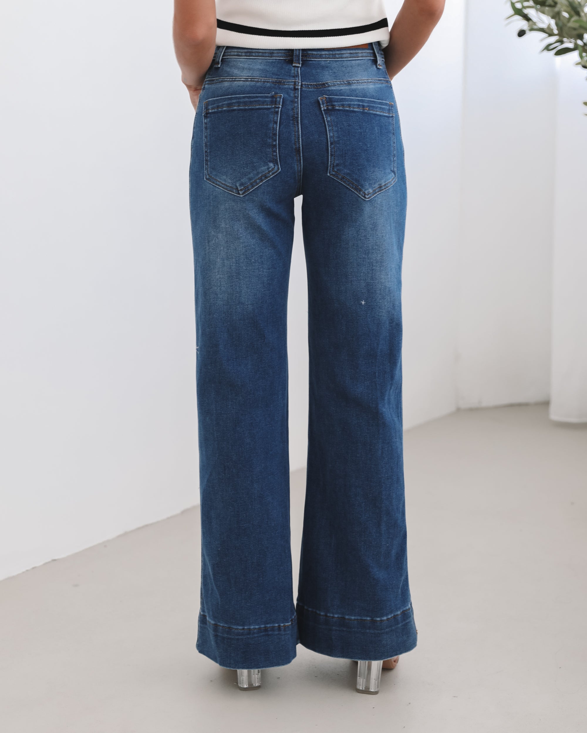 A woman standing in a room with light decor, wearing a striped top and mid-blue Yzabel Jeans with a high waist fit and wide leg silhouette.