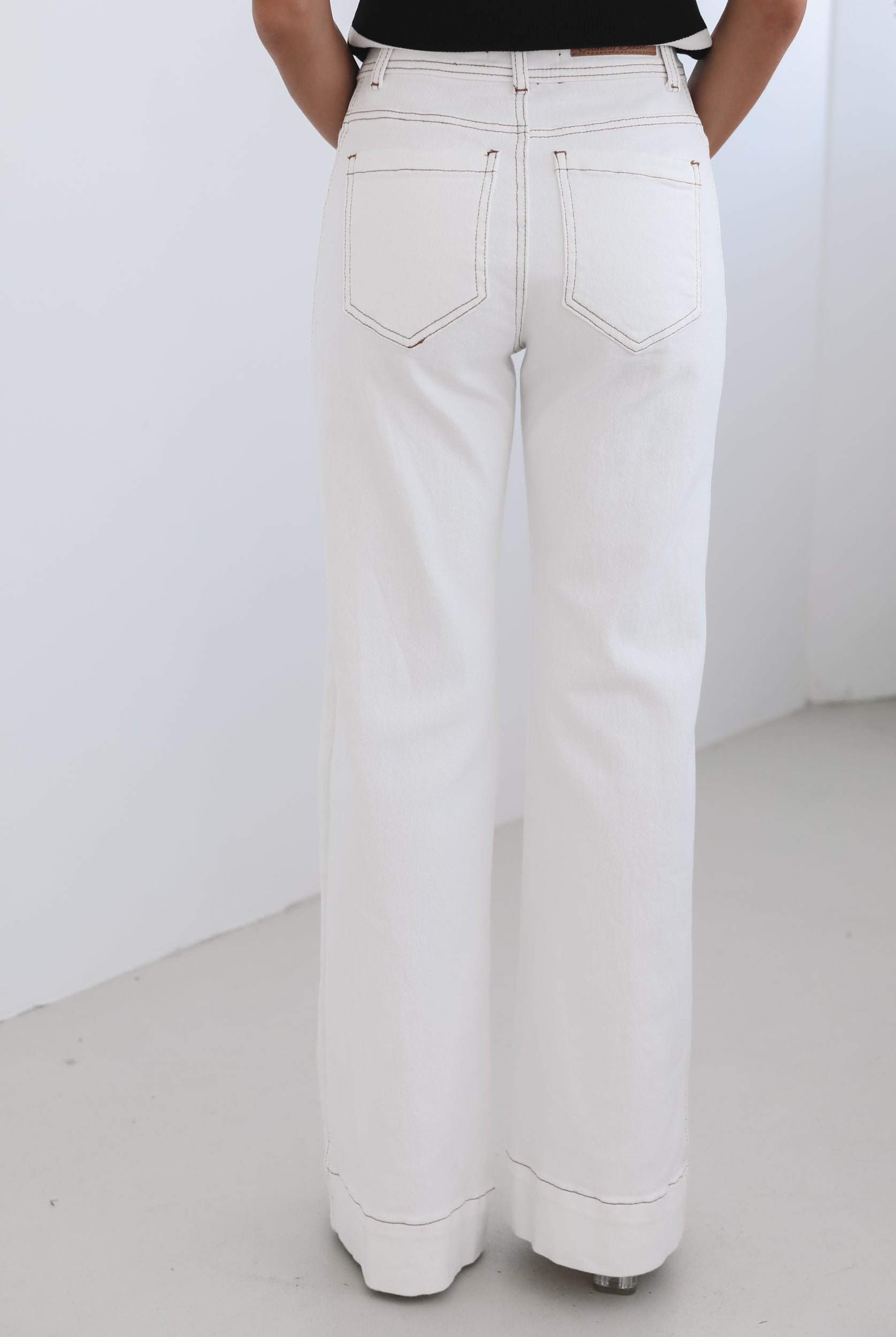 A female model wearing white high-waisted jeans with brown contrasting stitches, paired with a striped black and white top.