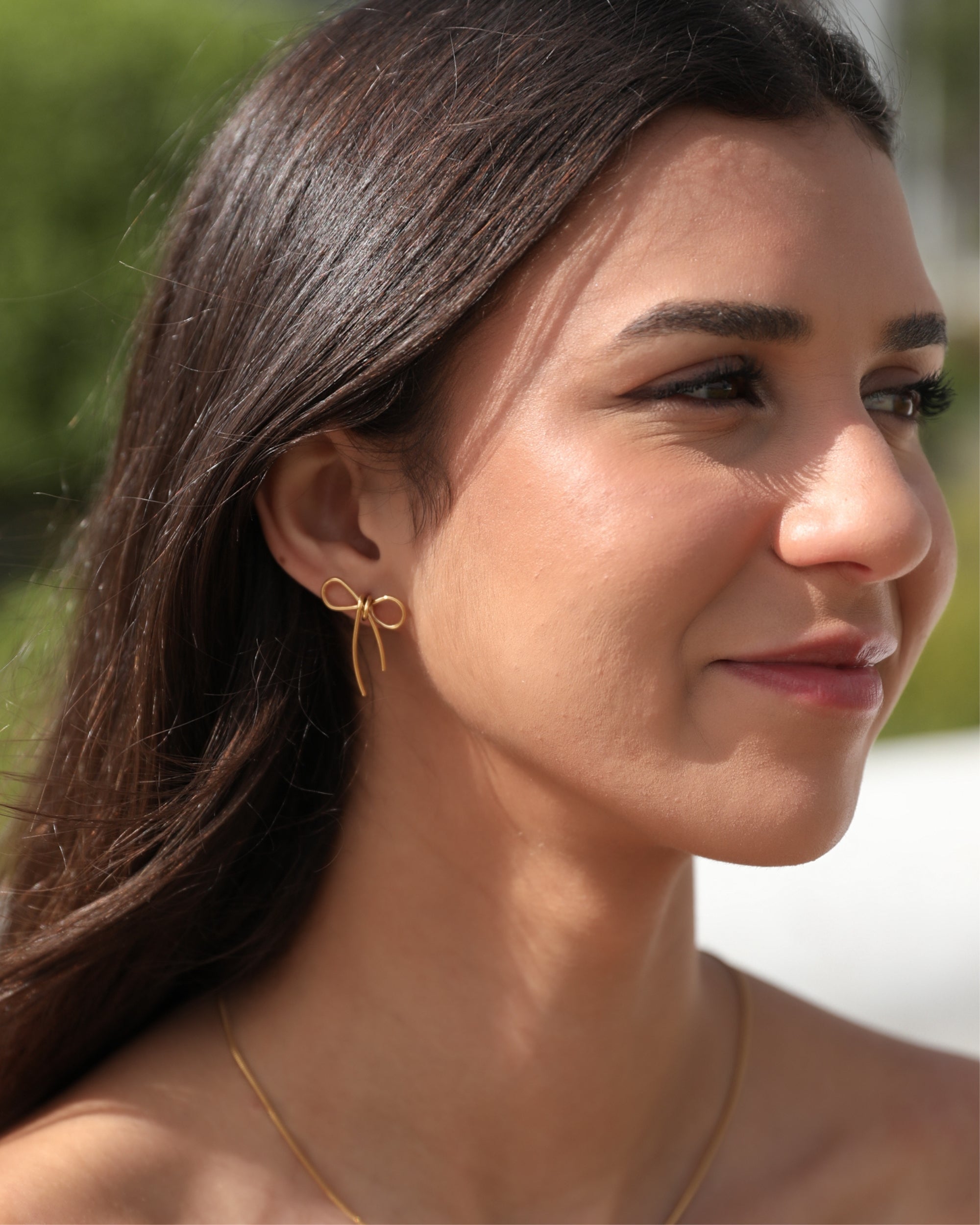 A person wearing gold bow-shaped earrings.