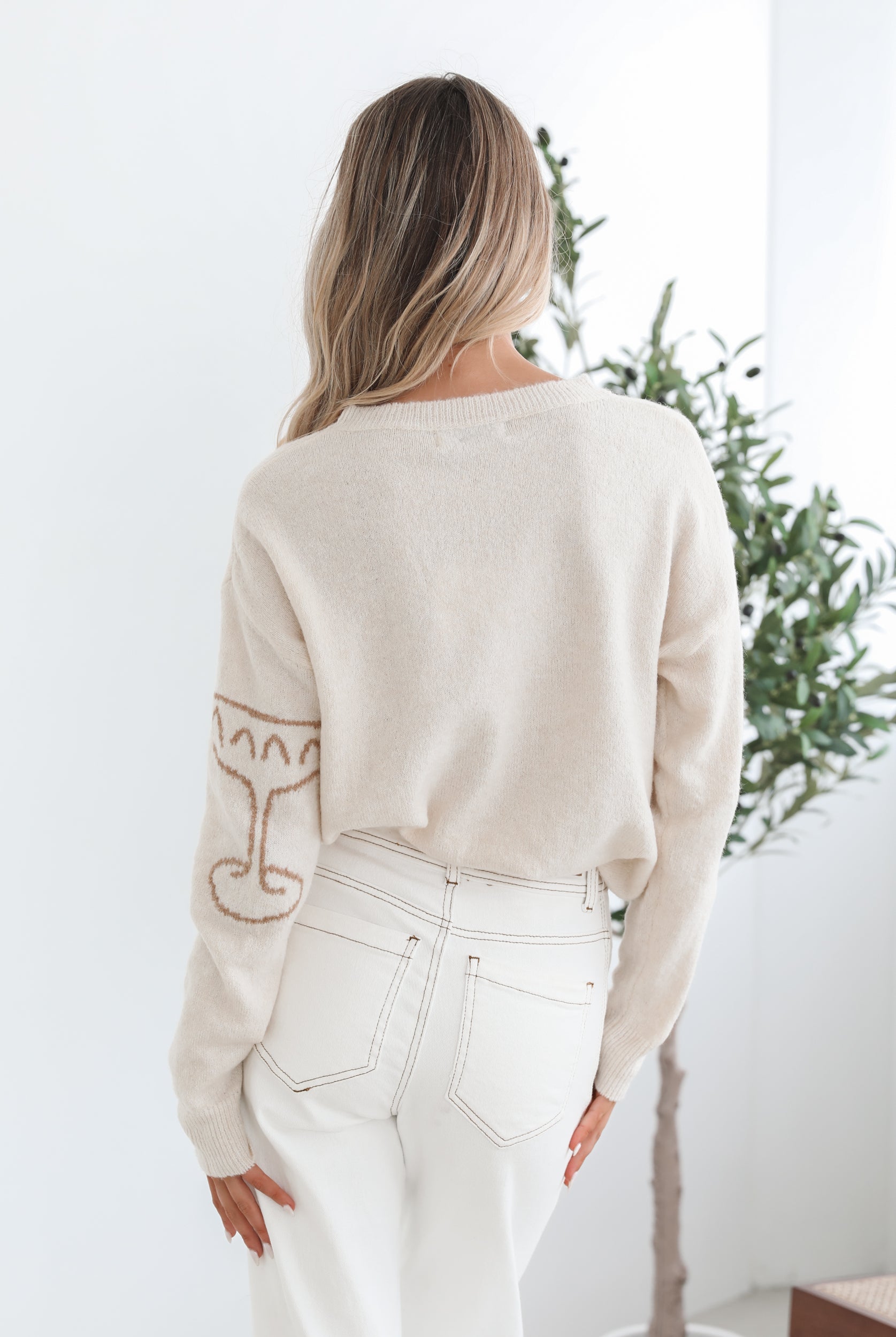 A woman wearing a cream-colored knit top with a round neckline and long sleeves, featuring a print of various items.