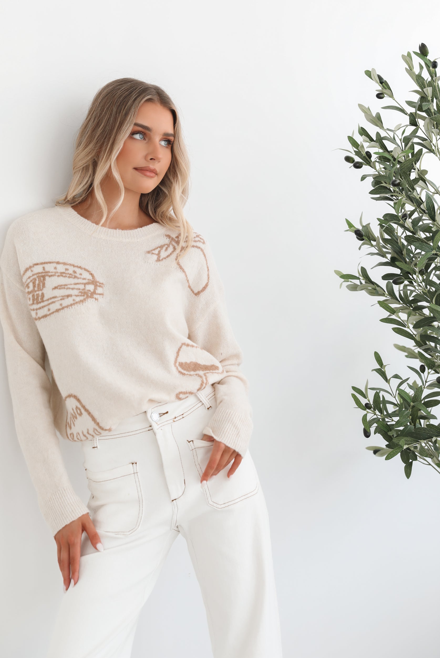 A woman wearing a cream-colored knit top with a round neckline and long sleeves, featuring a print of various items.