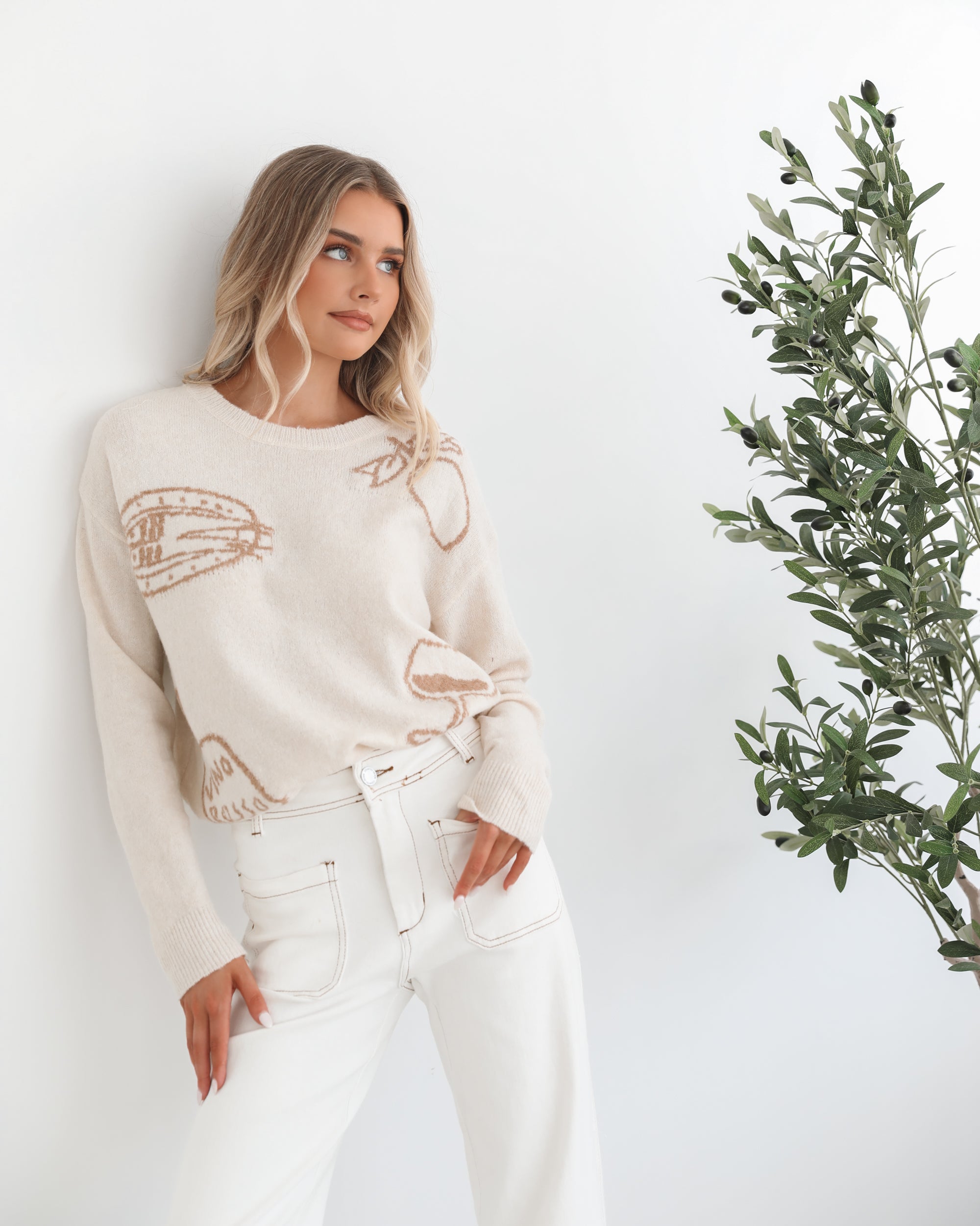 A woman wearing a cream-colored knit top with a round neckline and long sleeves, featuring a print of various items.
