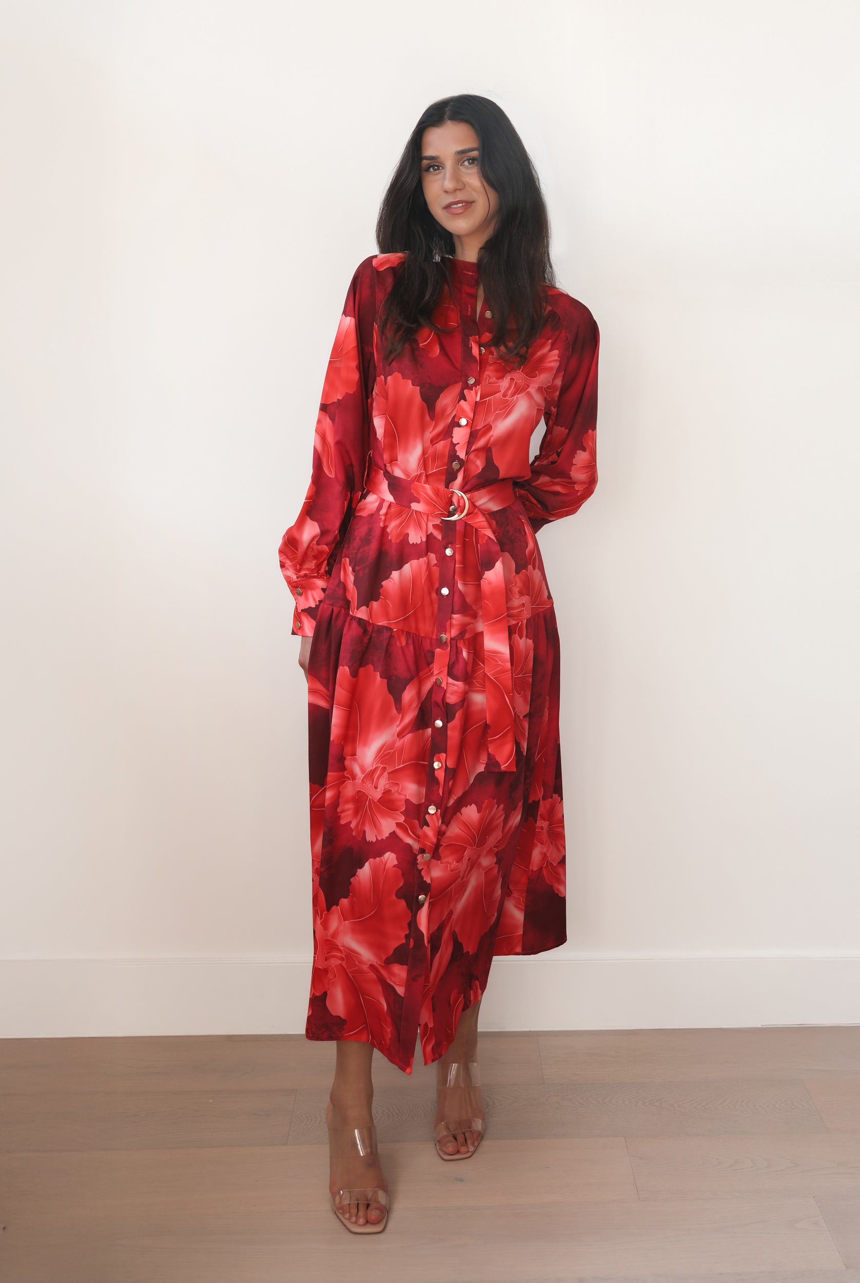 Woman wearing a red floral dress against a white wall