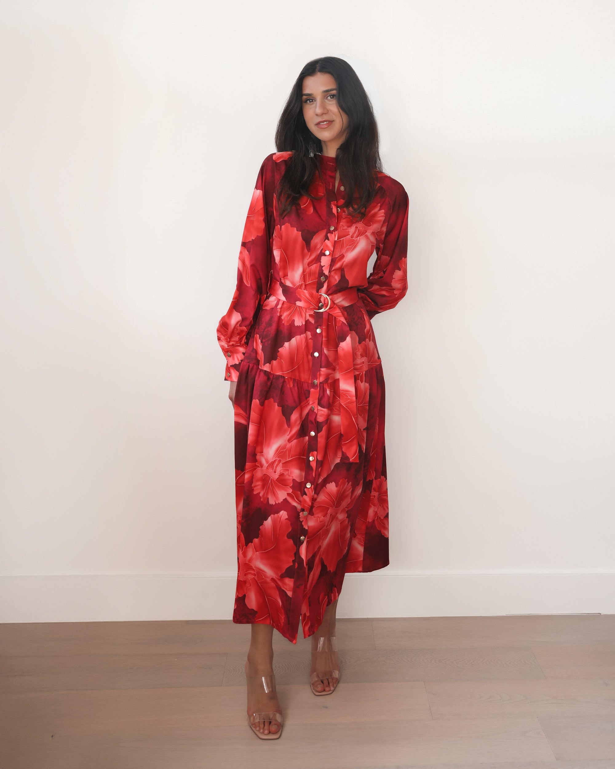 Woman wearing a red floral dress against a white wall