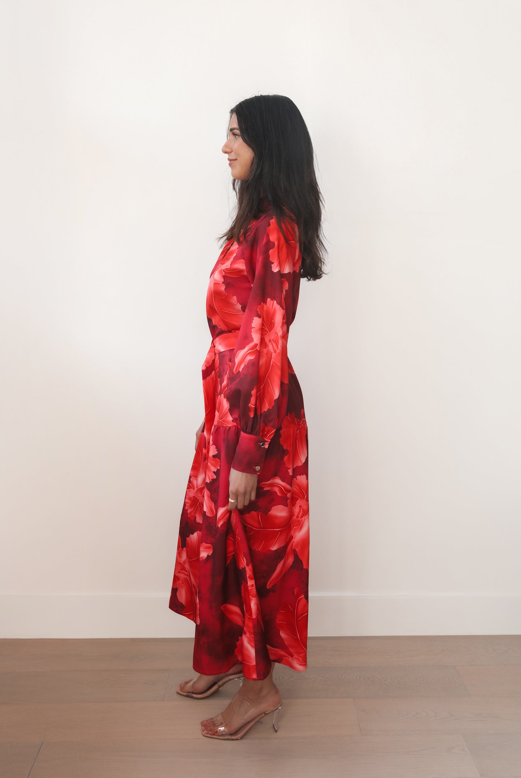 Woman wearing a red floral dress standing against a white wall.