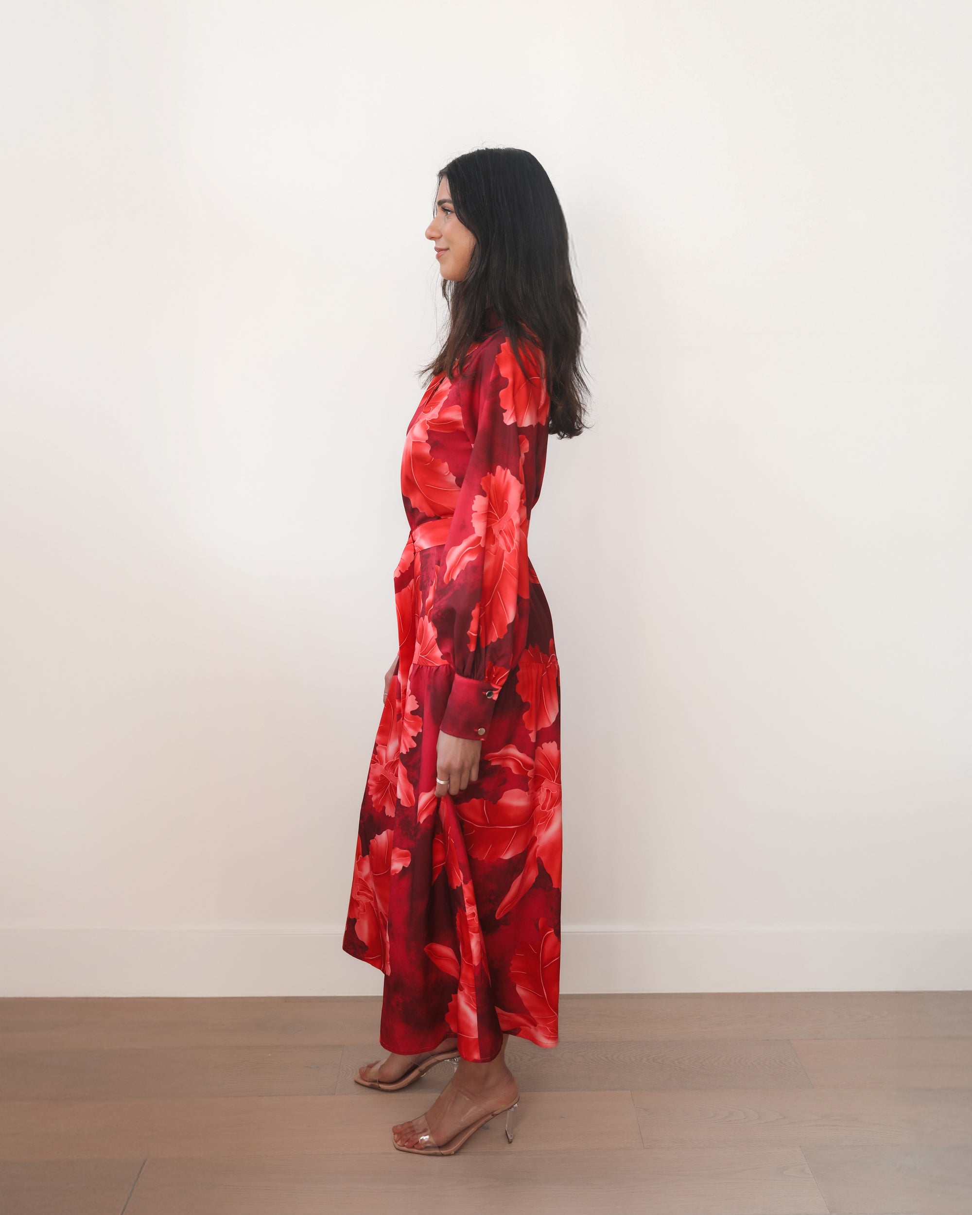 Woman wearing a red floral dress standing against a white wall.