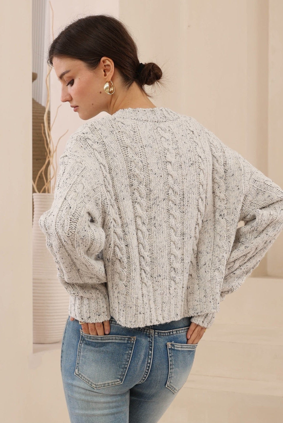 Woman wearing a cable knit sweater and jeans in a neutral setting