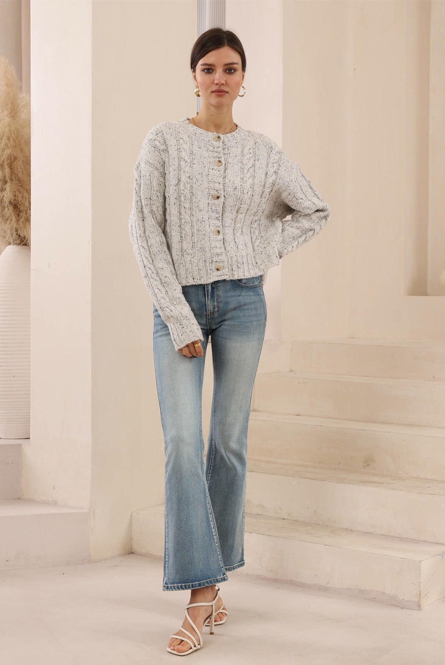 Woman wearing a light gray cardigan and blue jeans in a neutral setting