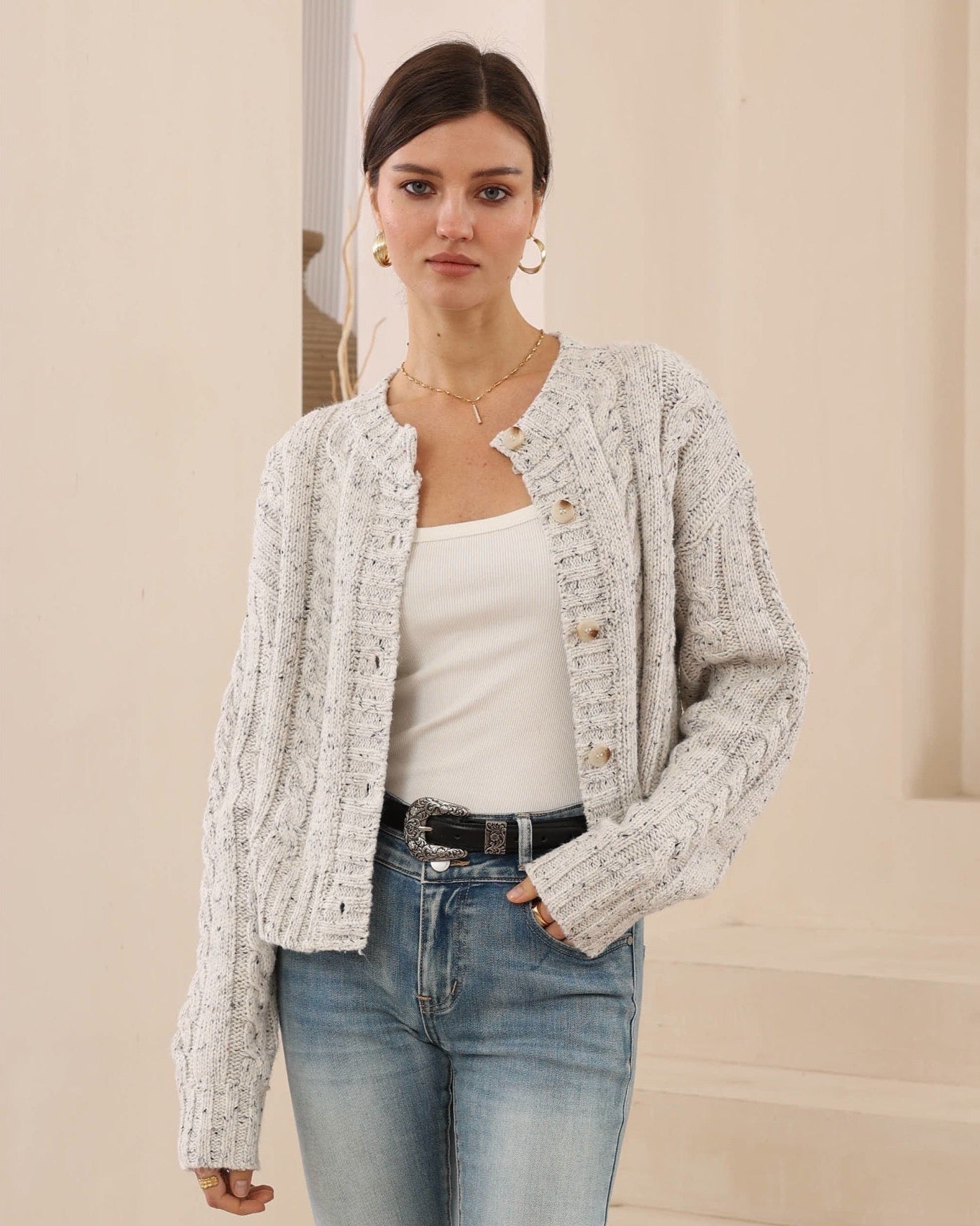 Woman wearing a textured cardigan over a white top and jeans against a neutral background