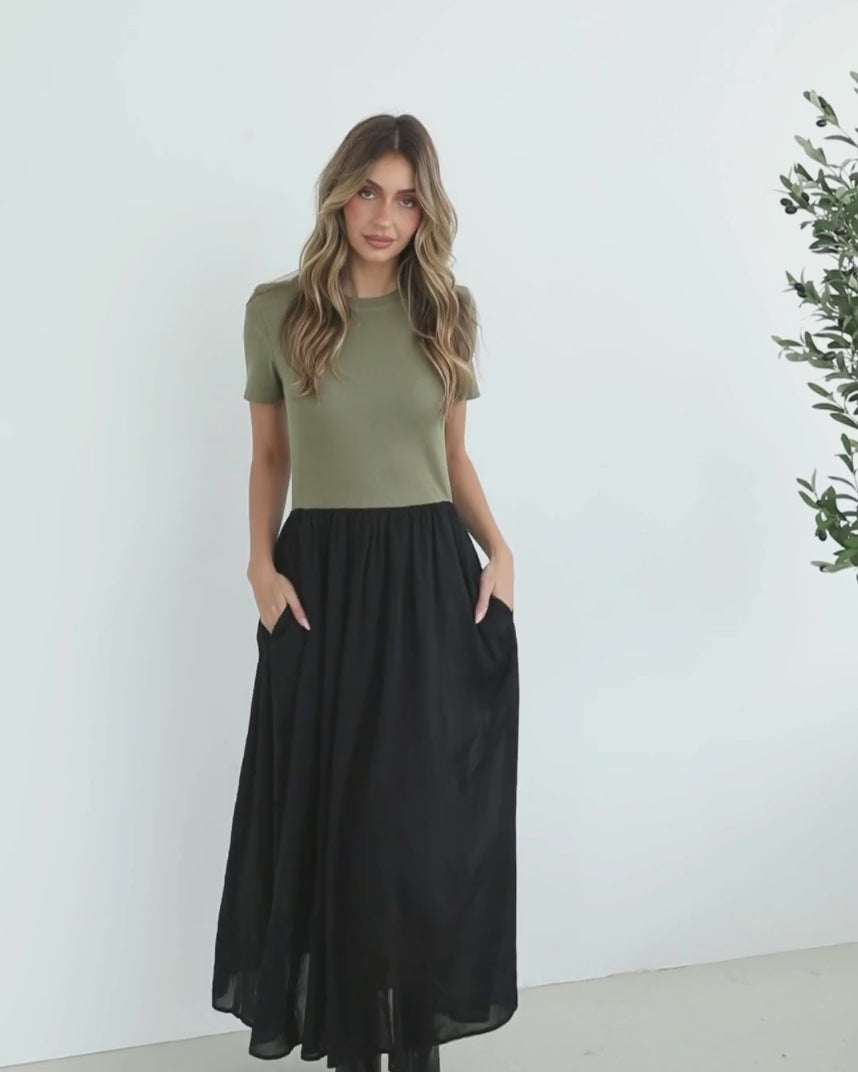 woman wearing a short sleeve round neck dress with green top and black flowy skirt paired with black boots in a white background studio