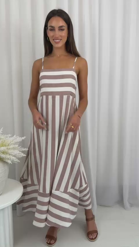Woman wearing a brown and white striped dress against a white curtain background