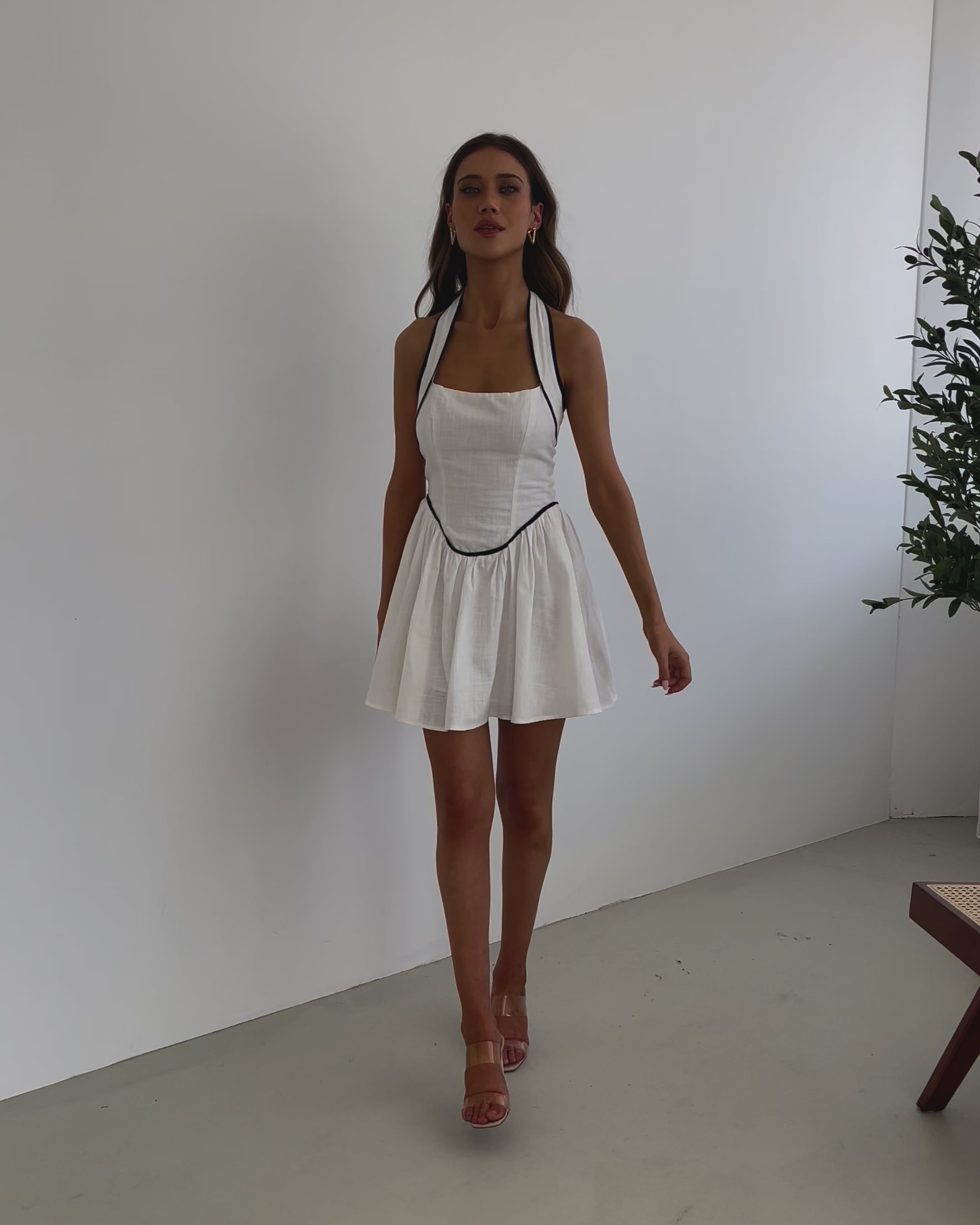 A woman wearing a white mini dress with a halter neck strap and contrasting black piping.
