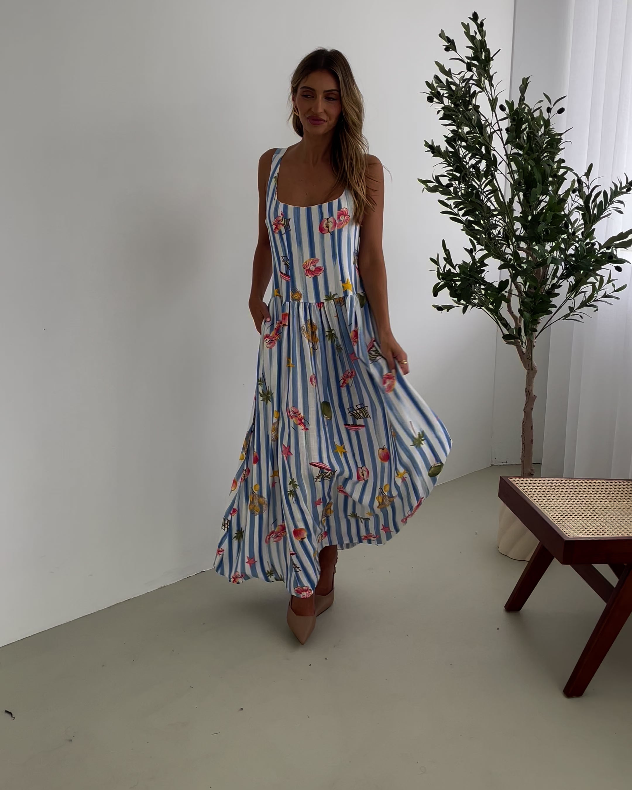 A model wearing a white and blue base multicolored print maxi dress with a square neckline and wide straps.