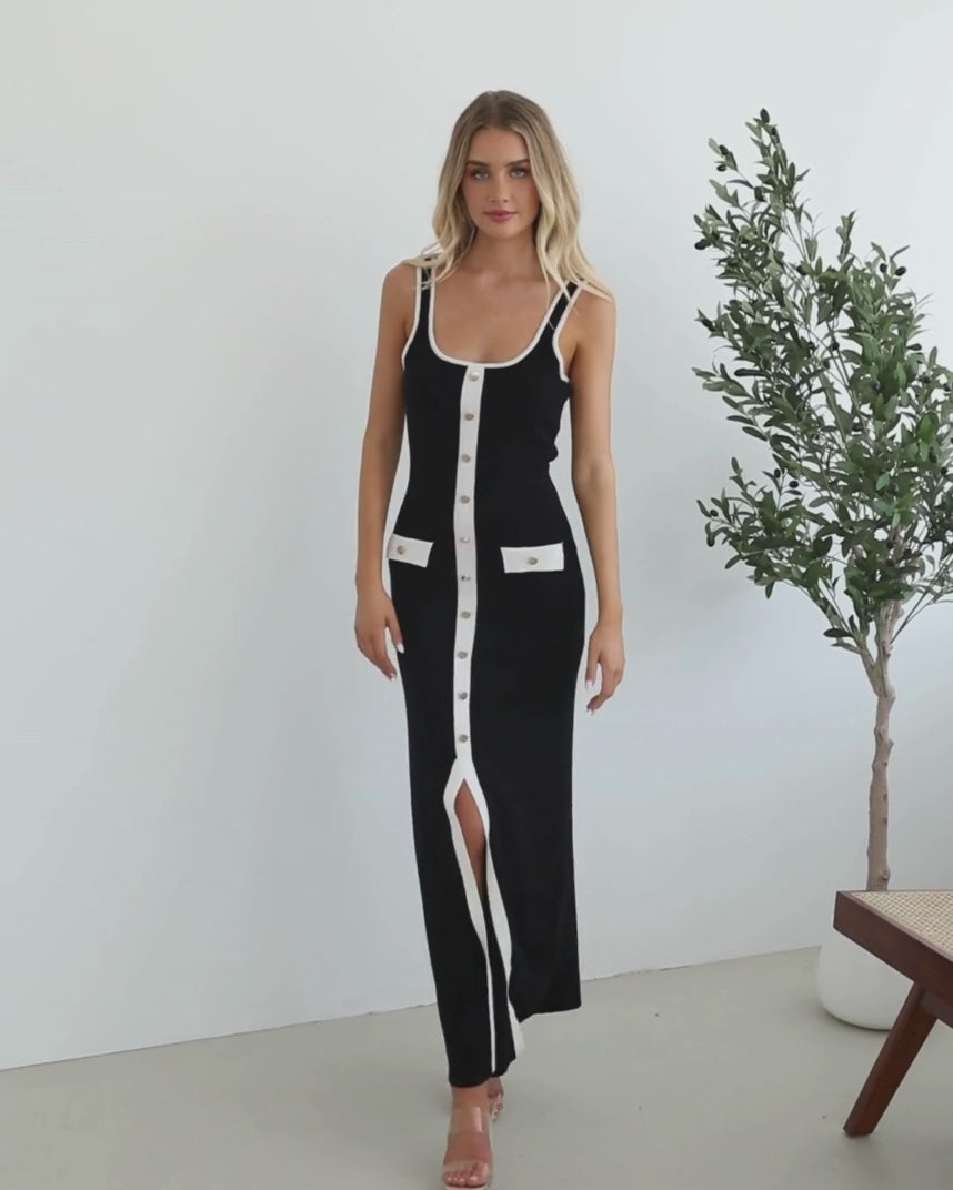 A model wearing a black sleeveless knit dress with a scoop neckline, center-front buttons, and a maxi length hem.