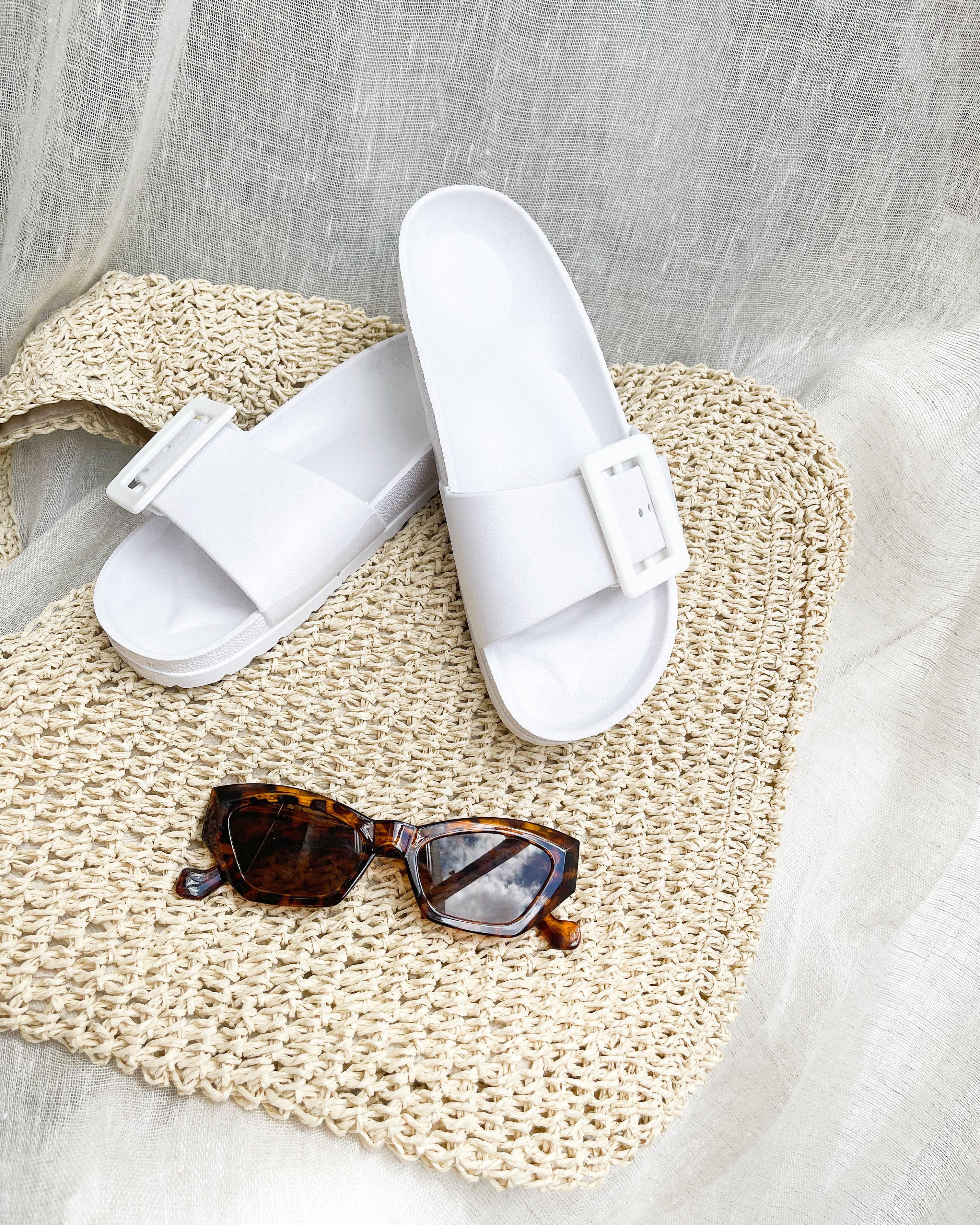 A pair of black summer slides with thick straps, displayed on a flat surface with a knitted texture in the background.