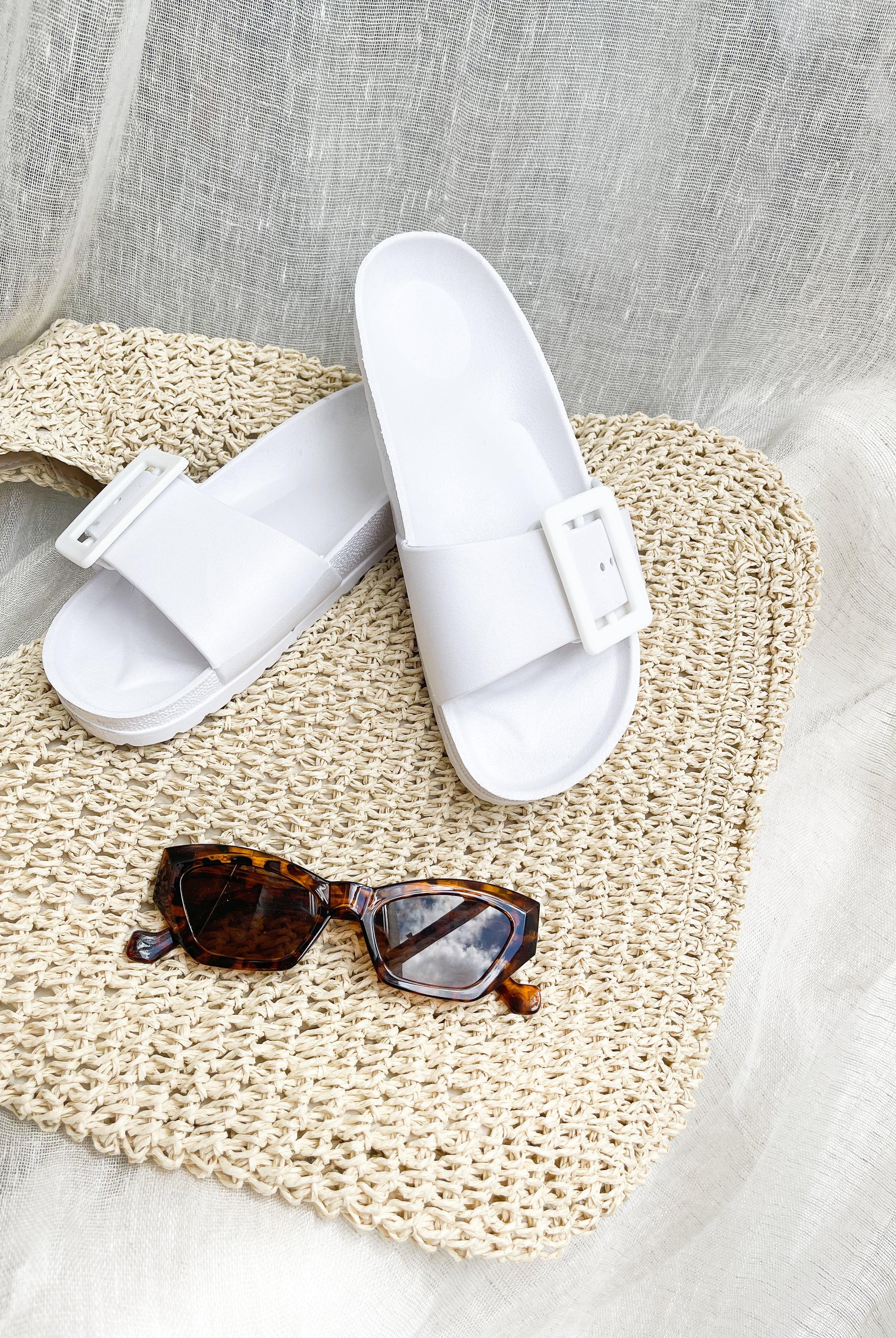 A pair of black summer slides with thick straps, displayed on a flat surface with a knitted texture in the background.