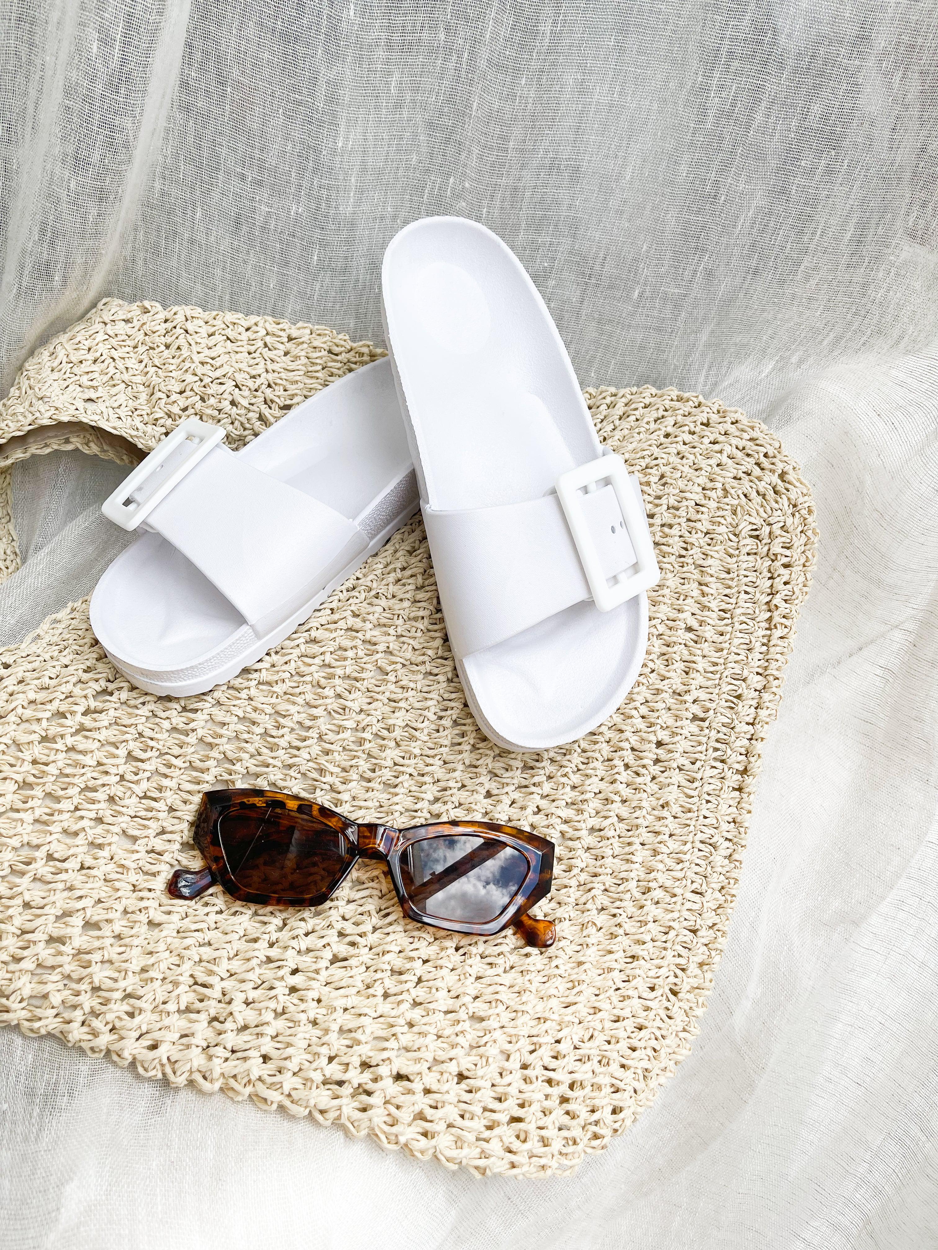 A pair of black summer slides with thick straps, displayed on a flat surface with a knitted texture in the background.