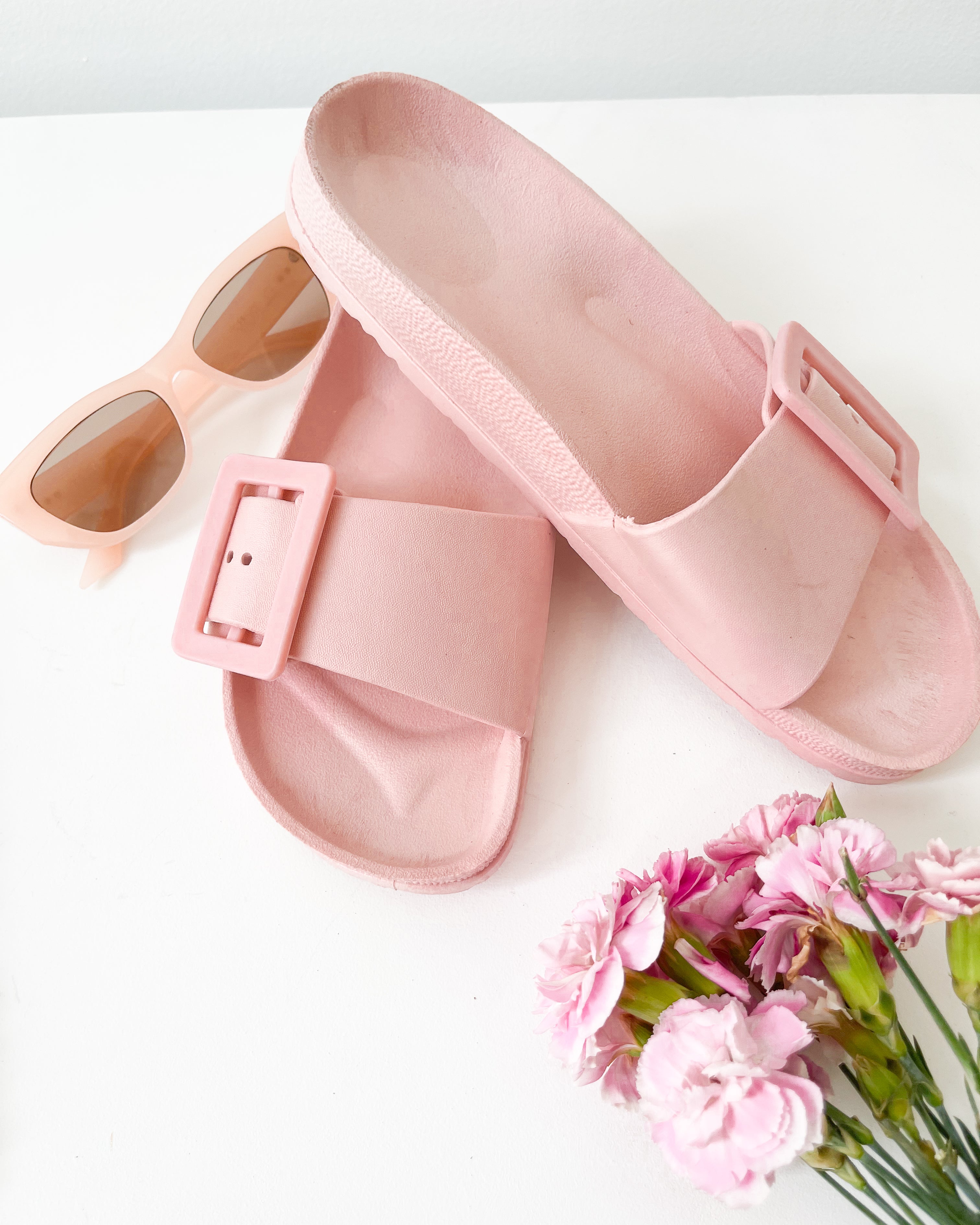 A pair of black summer slides with thick straps, displayed on a flat surface with a knitted texture in the background.