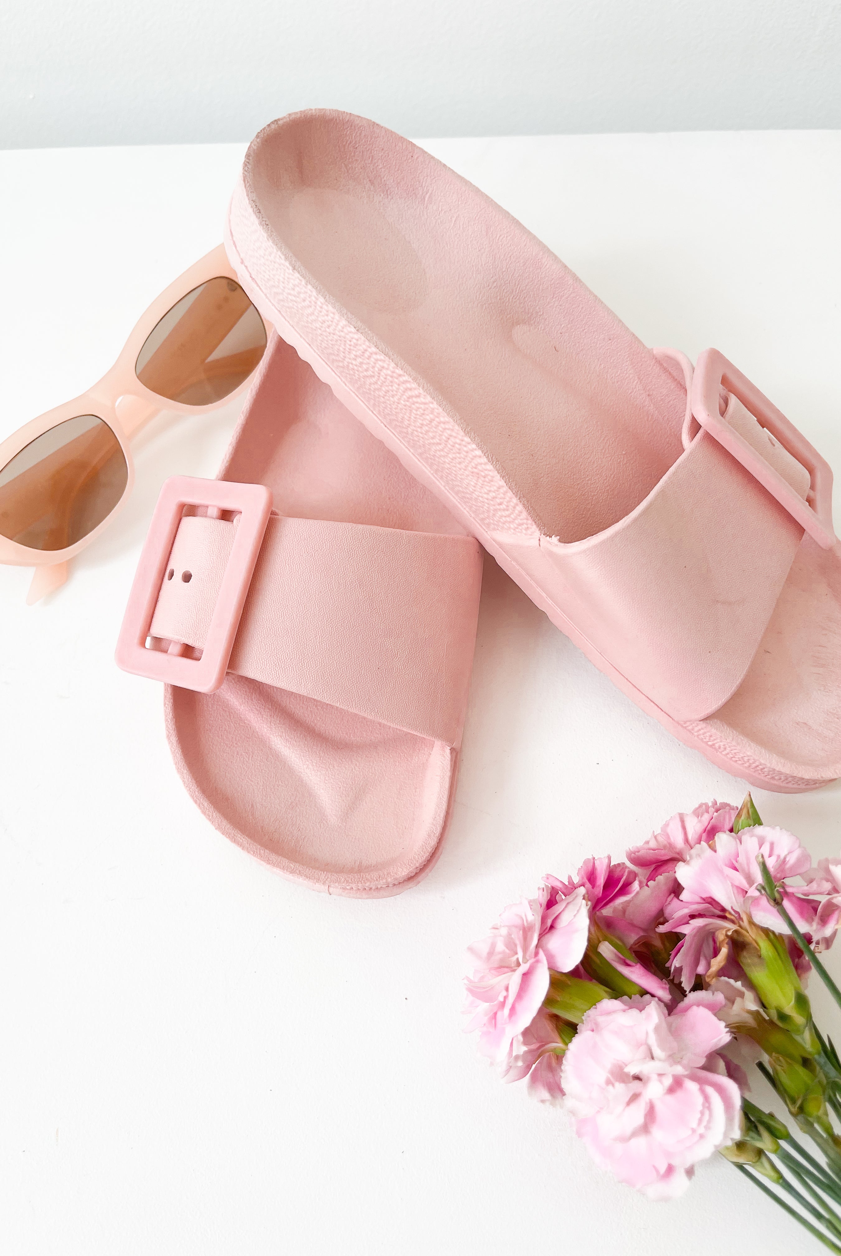 A pair of black summer slides with thick straps, displayed on a flat surface with a knitted texture in the background.