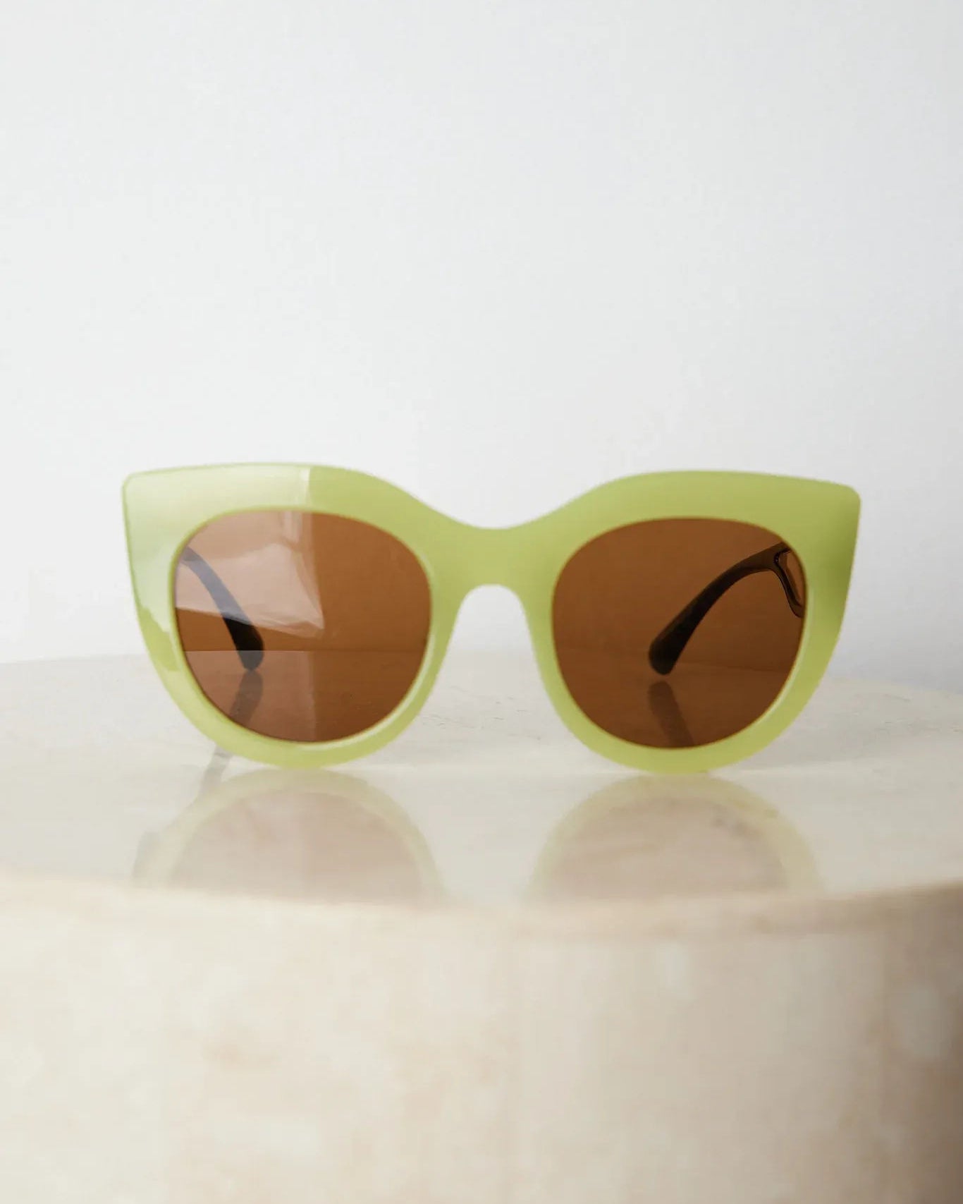 A pair of sunglasses with green frames and brown lenses displayed on a surface.