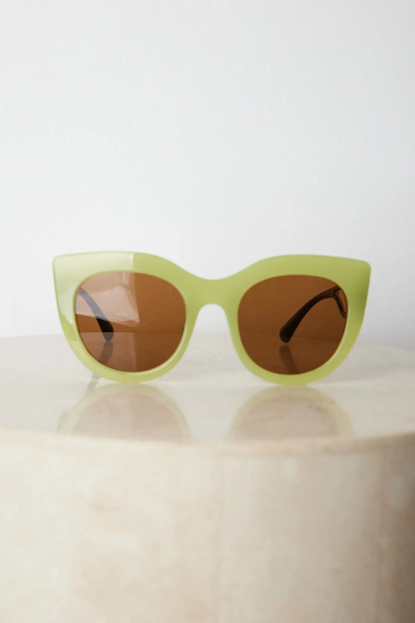 A pair of sunglasses with green frames and brown lenses displayed on a surface.