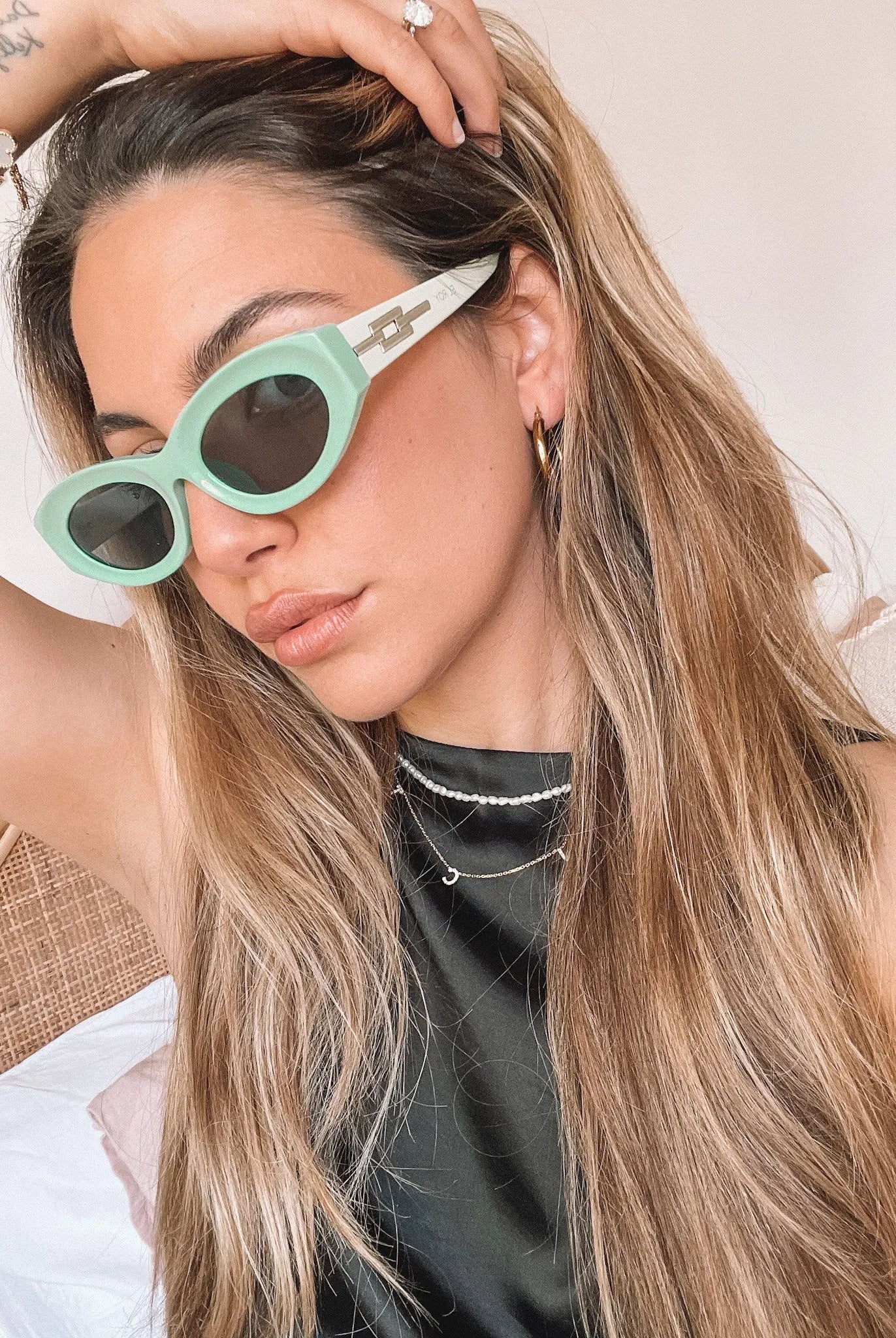Close-up of a pair of bright green cat-eye sunglasses with dark lenses, placed on a smooth beige surface with a plain white background.
