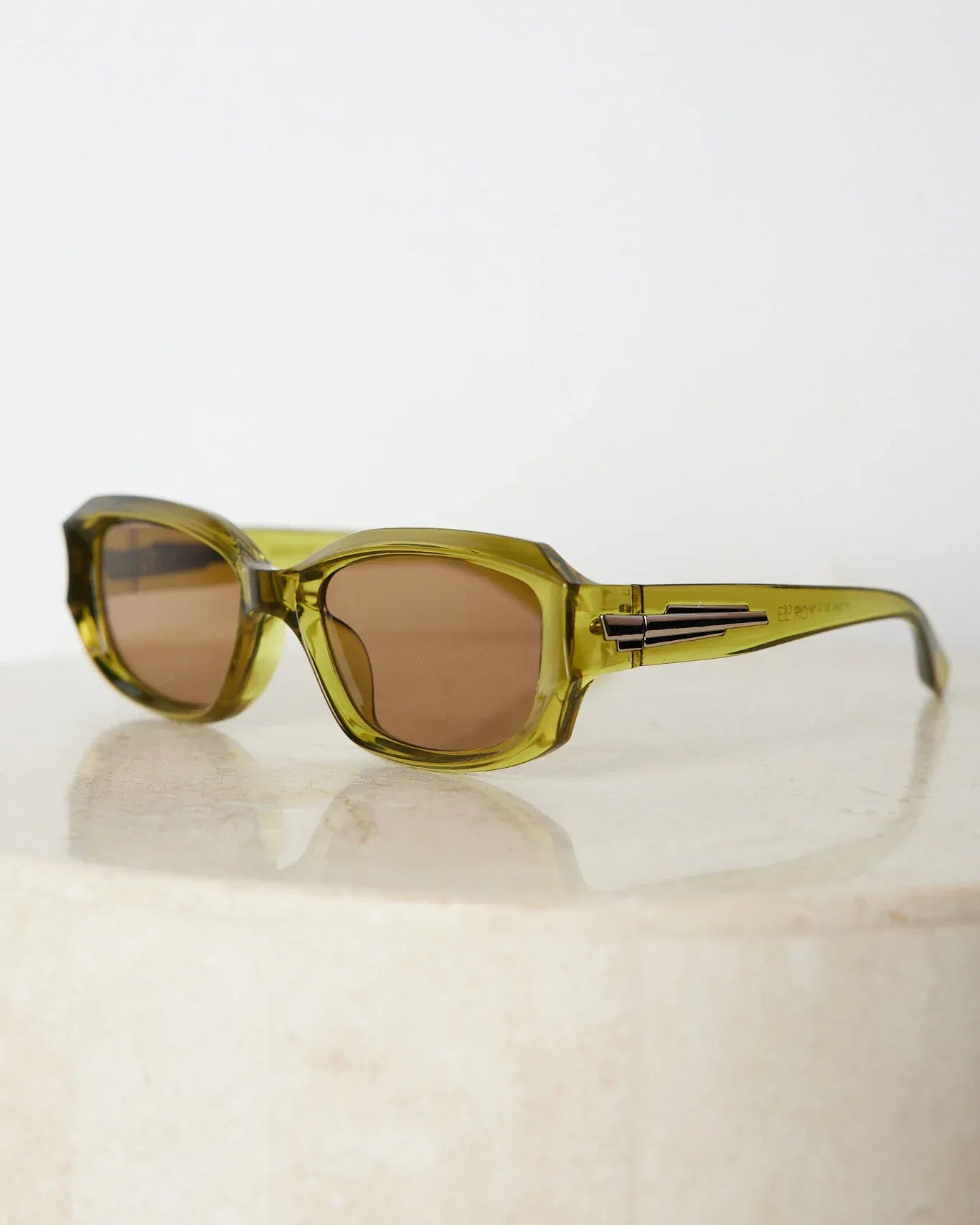 Rectangular sunglasses with translucent olive green frames and brown tinted lenses, displayed on a light beige stone surface against a plain white background.