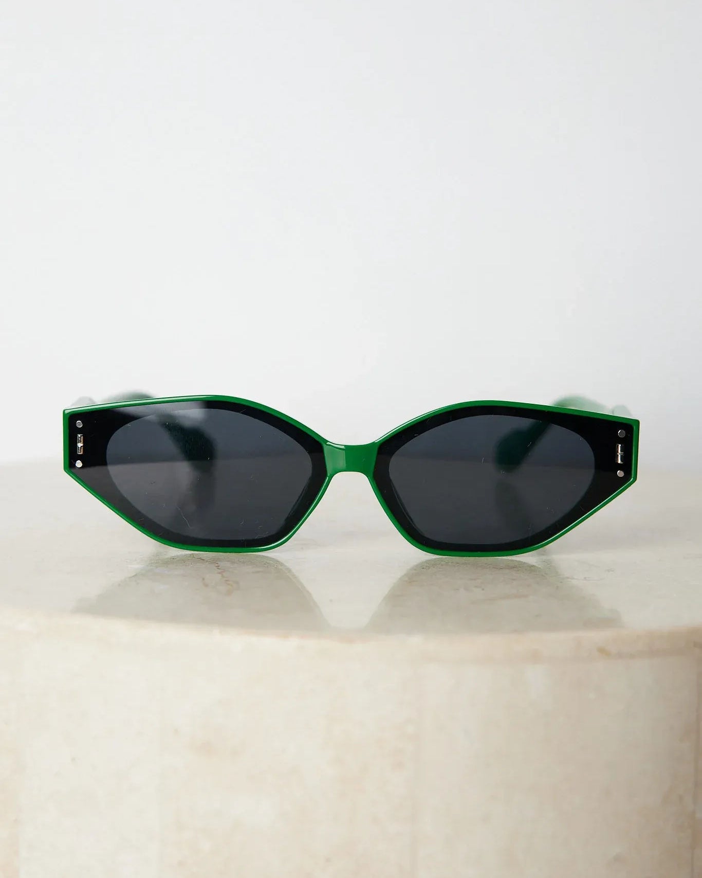 Green geometric-shaped sunglasses with dark lenses resting on a light marble surface against a plain white background.