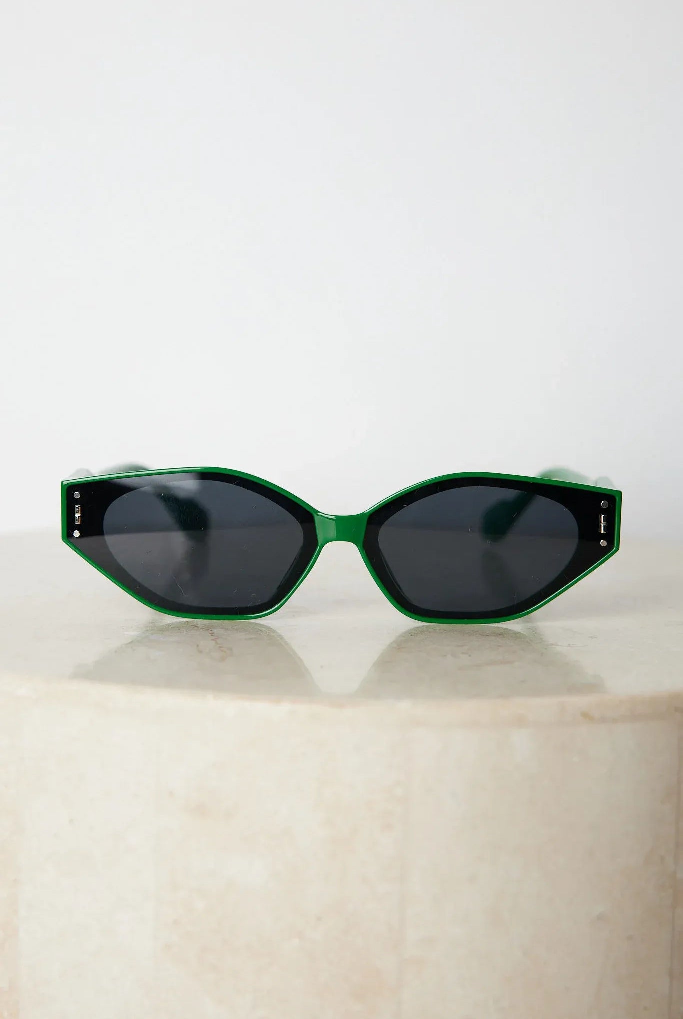 Green geometric-shaped sunglasses with dark lenses resting on a light marble surface against a plain white background.