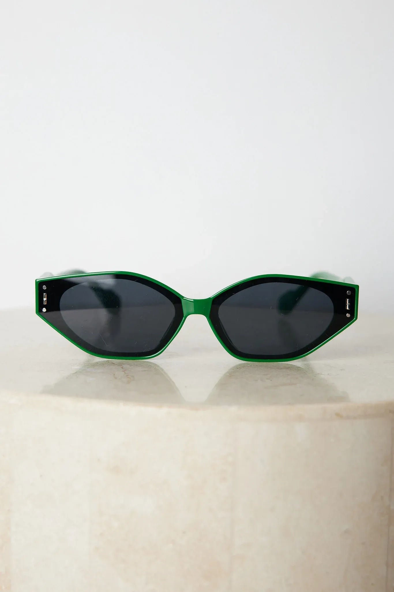 Green geometric-shaped sunglasses with dark lenses resting on a light marble surface against a plain white background.