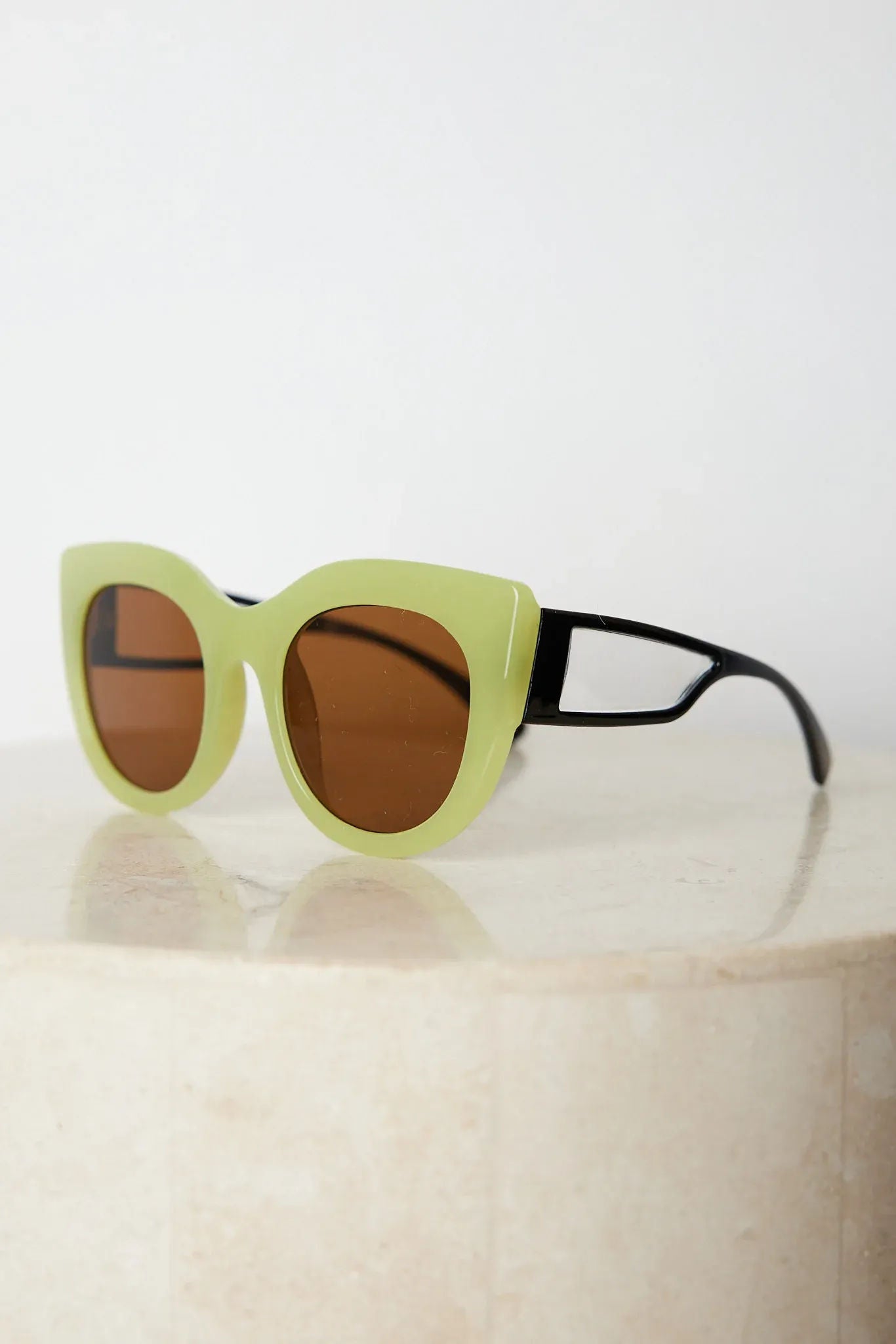 A pair of sunglasses with green frames and brown lenses displayed on a surface.