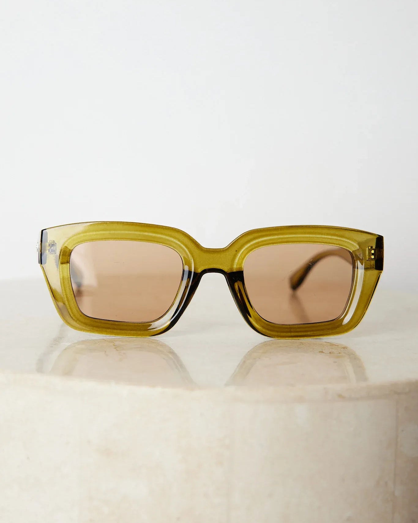 A pair of sunglasses with olive green frames and pink lenses displayed on a surface.