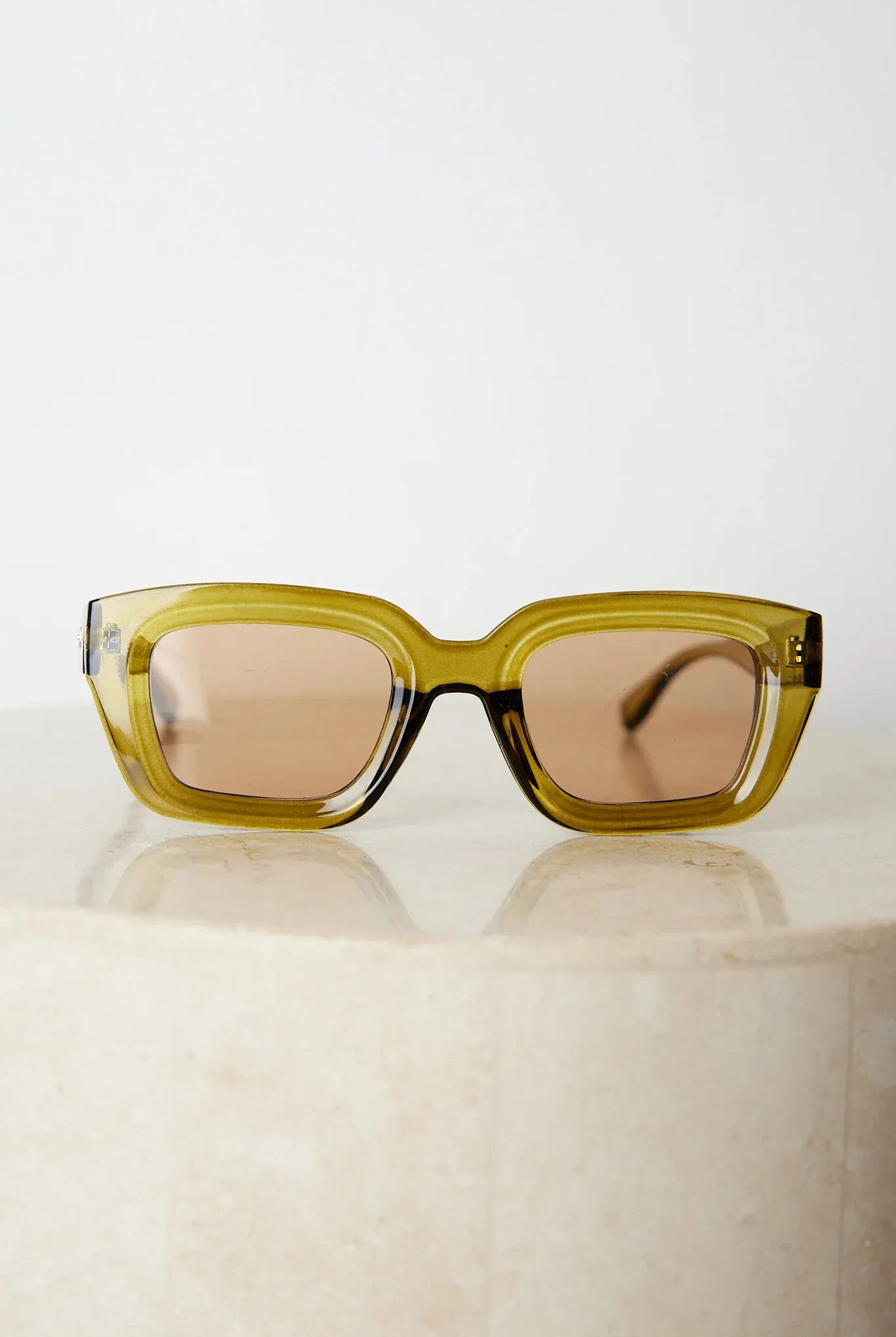 A pair of sunglasses with olive green frames and pink lenses displayed on a surface.