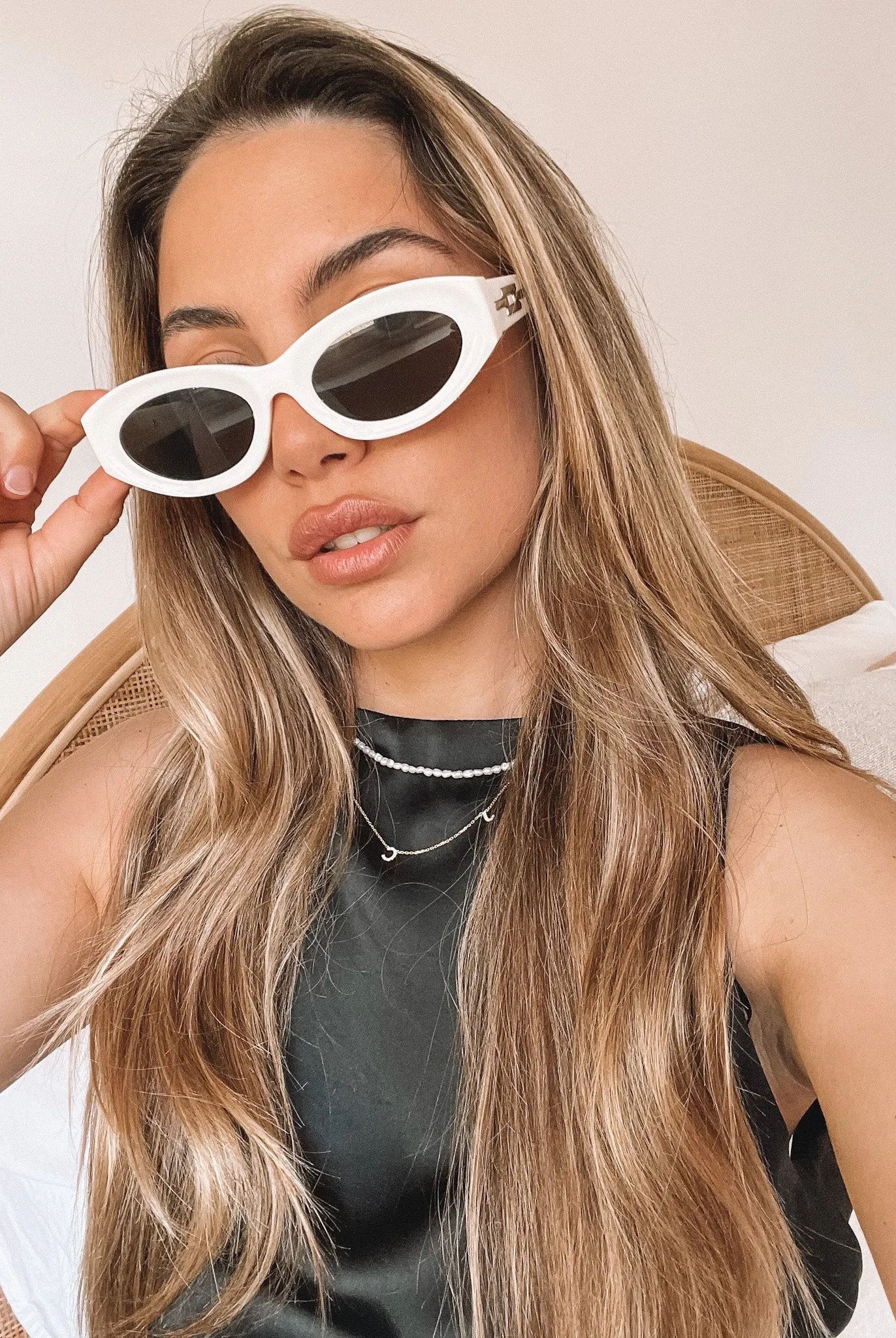 Close-up of a pair of white oval-shaped sunglasses with dark lenses, resting on a smooth beige surface against a plain white background.