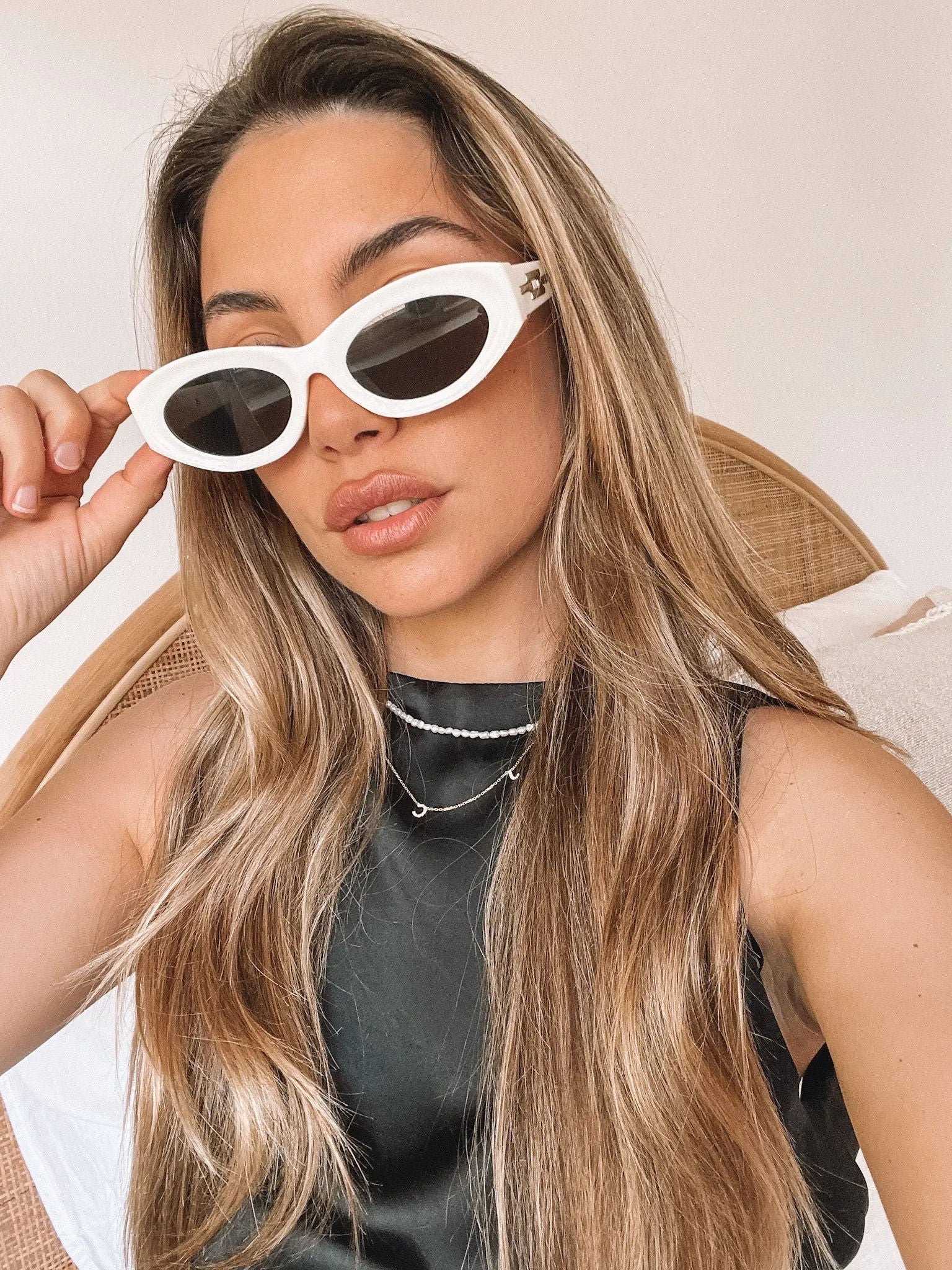 Close-up of a pair of white oval-shaped sunglasses with dark lenses, resting on a smooth beige surface against a plain white background.