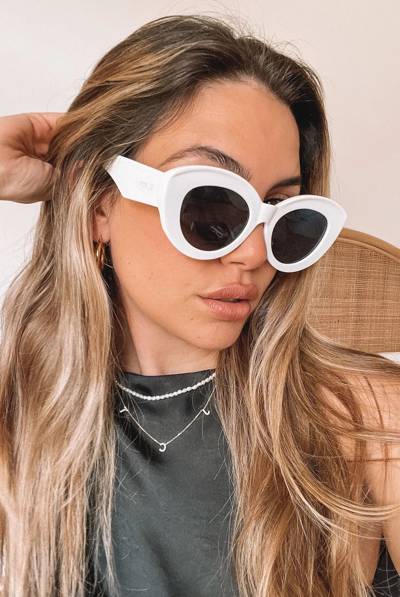 White cat-eye sunglasses with dark lenses displayed on a light beige marble surface against a plain white background.