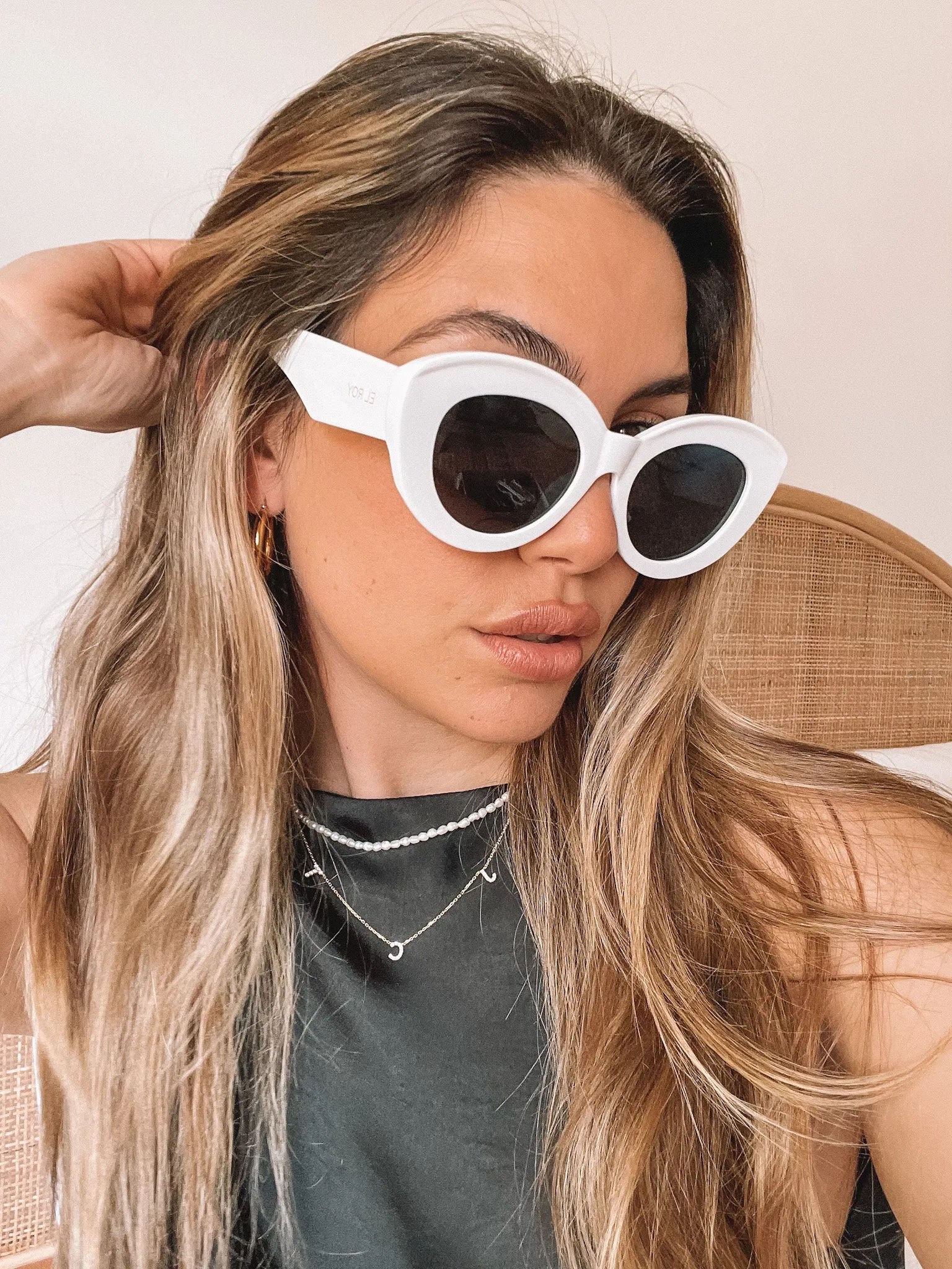 White cat-eye sunglasses with dark lenses displayed on a light beige marble surface against a plain white background.