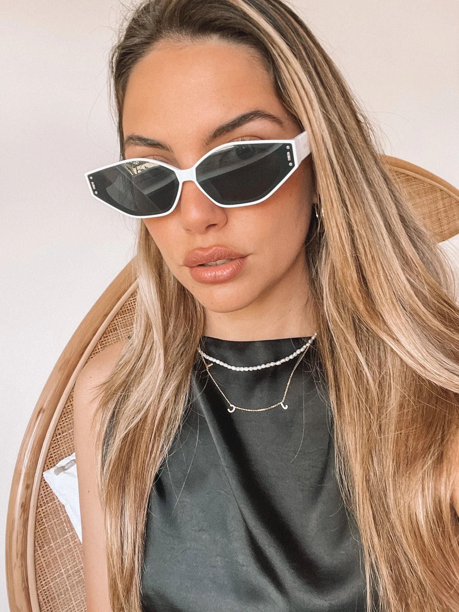 White geometric-shaped sunglasses with dark lenses resting on a light marble surface against a plain white background.