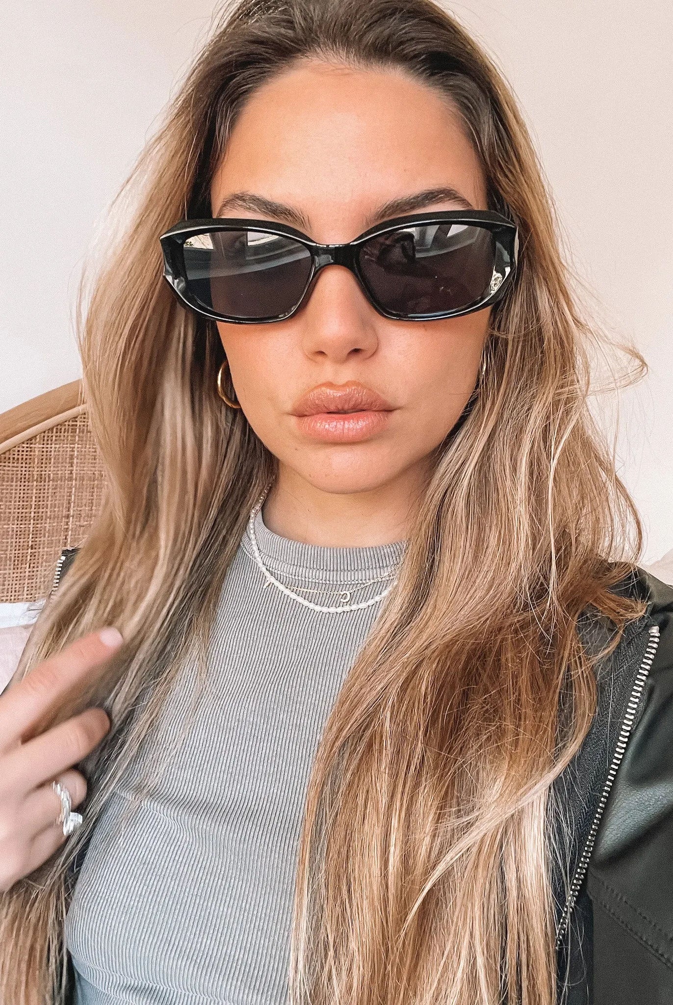 Black rectangular sunglasses with a glossy frame and dark tinted lenses, displayed on a light beige curved surface against a plain white background.