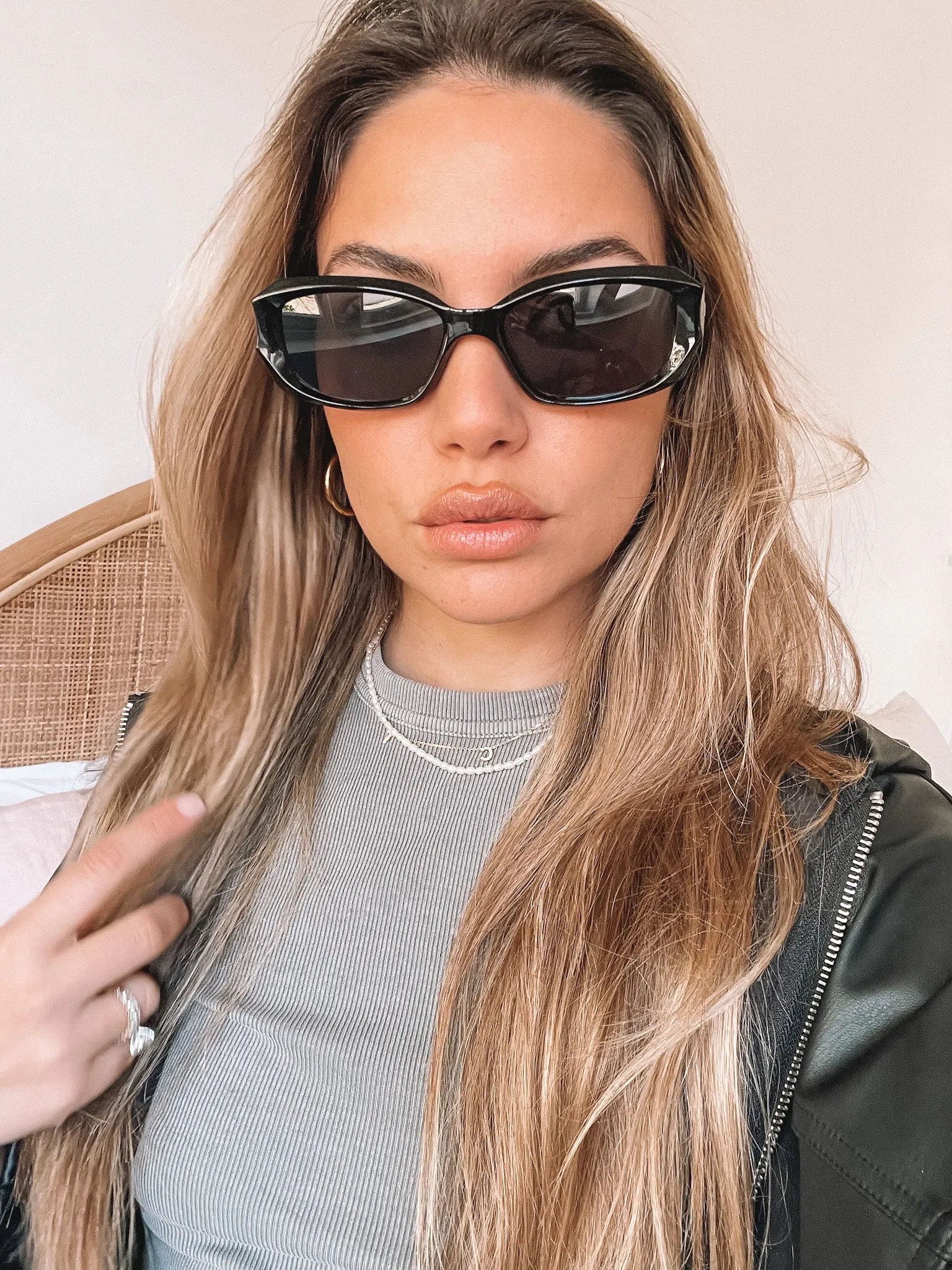 Black rectangular sunglasses with a glossy frame and dark tinted lenses, displayed on a light beige curved surface against a plain white background.