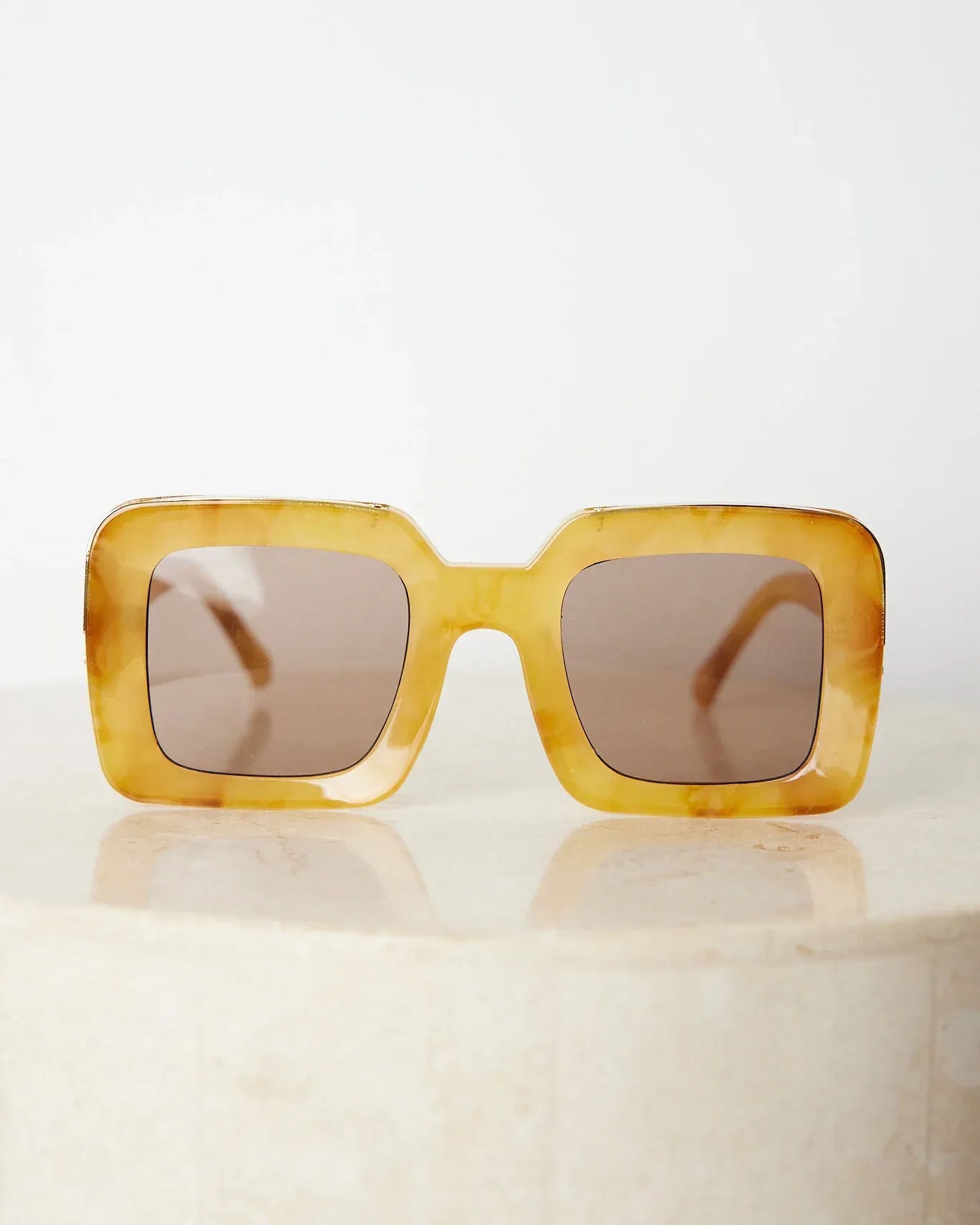 A pair of sunglasses with a tan frame displayed on a surface.
