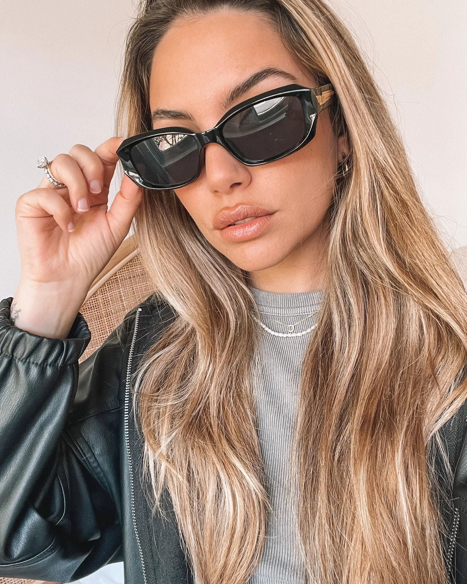 Black rectangular sunglasses with a glossy frame and dark tinted lenses, displayed on a light beige curved surface against a plain white background.
